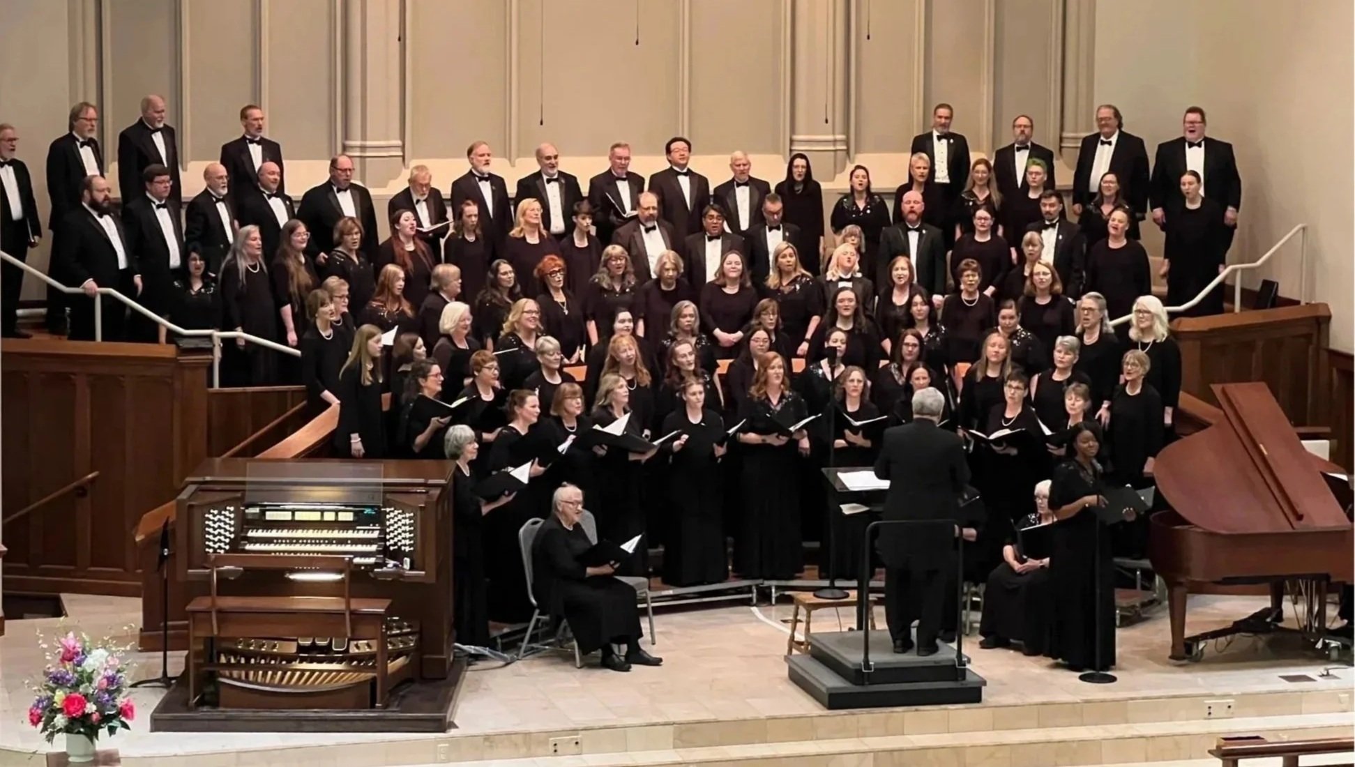 May 2026 photograph of 90-member combined chorus of Lawrence Civic Choir with William Baker Festival Singers in concert attire on church alter with Dr. William Baker conducting.