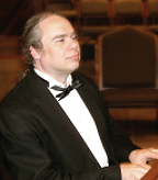 Photograph of Dr. Geoffrey Wilcken playing piano dressed in a tuxedo.