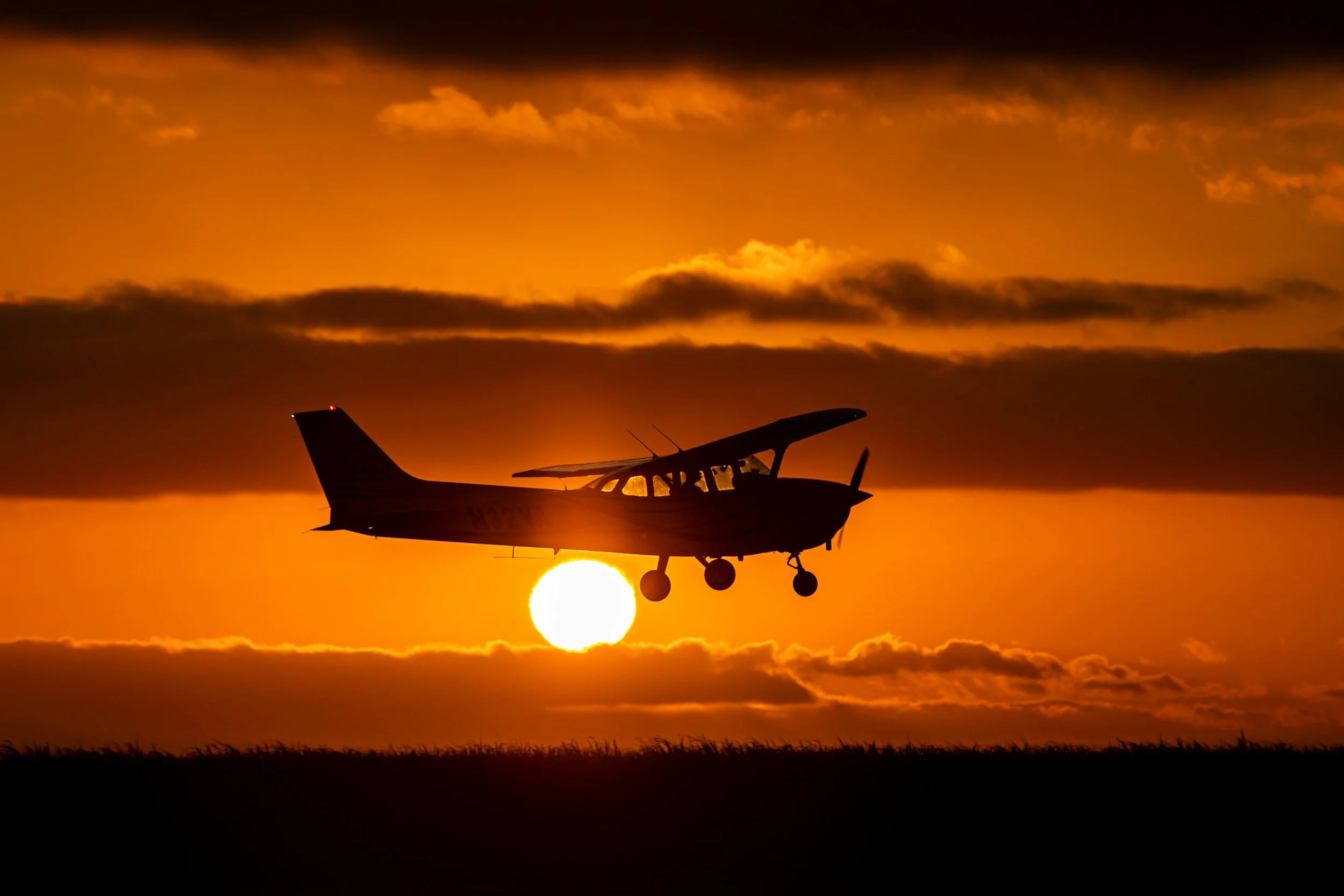 Small airplane flying in front of a setting sun with orange and dark clouds in the sky.