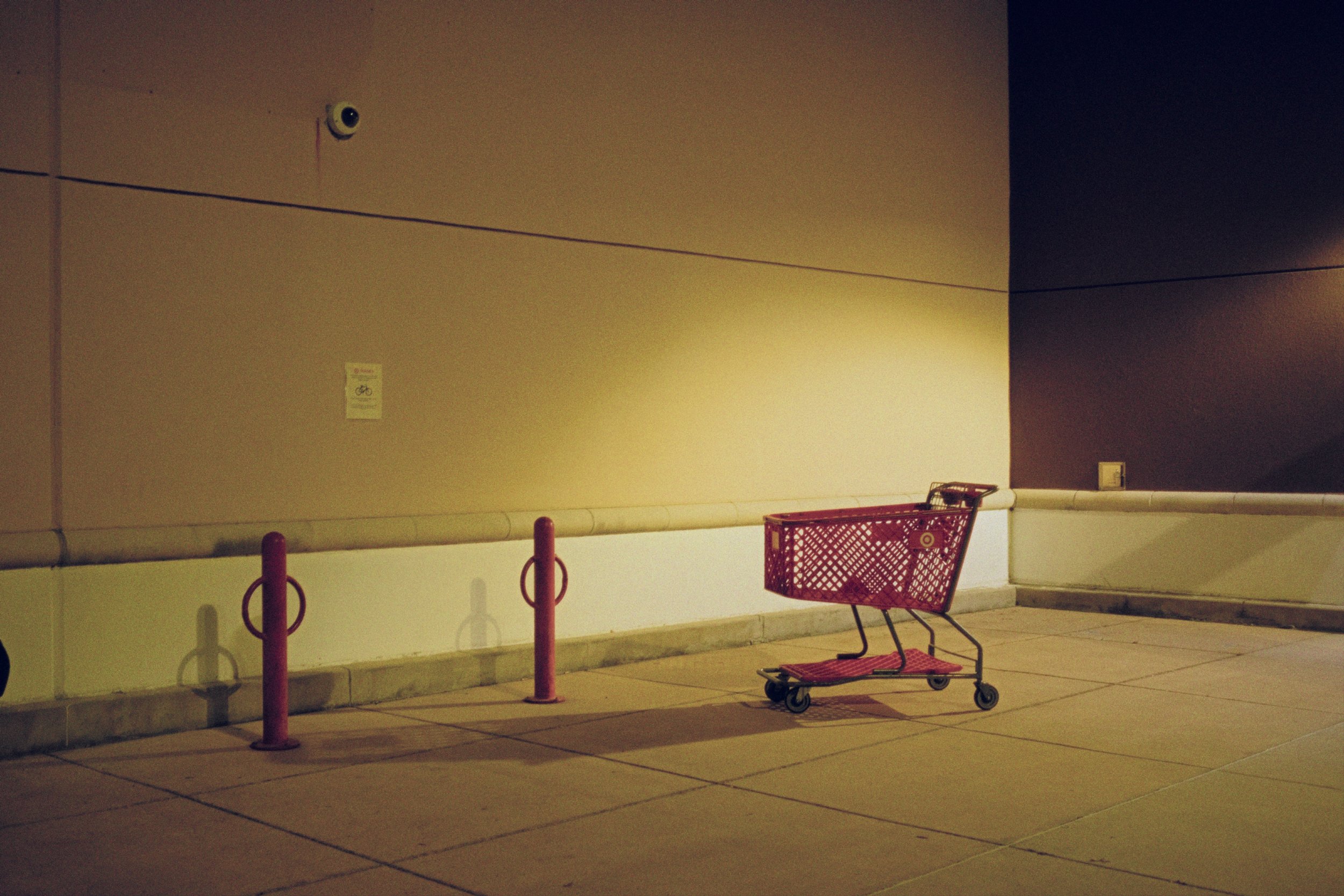 Empty shopping cart with a Target logo, lined up against a beige wall outside a store at night.