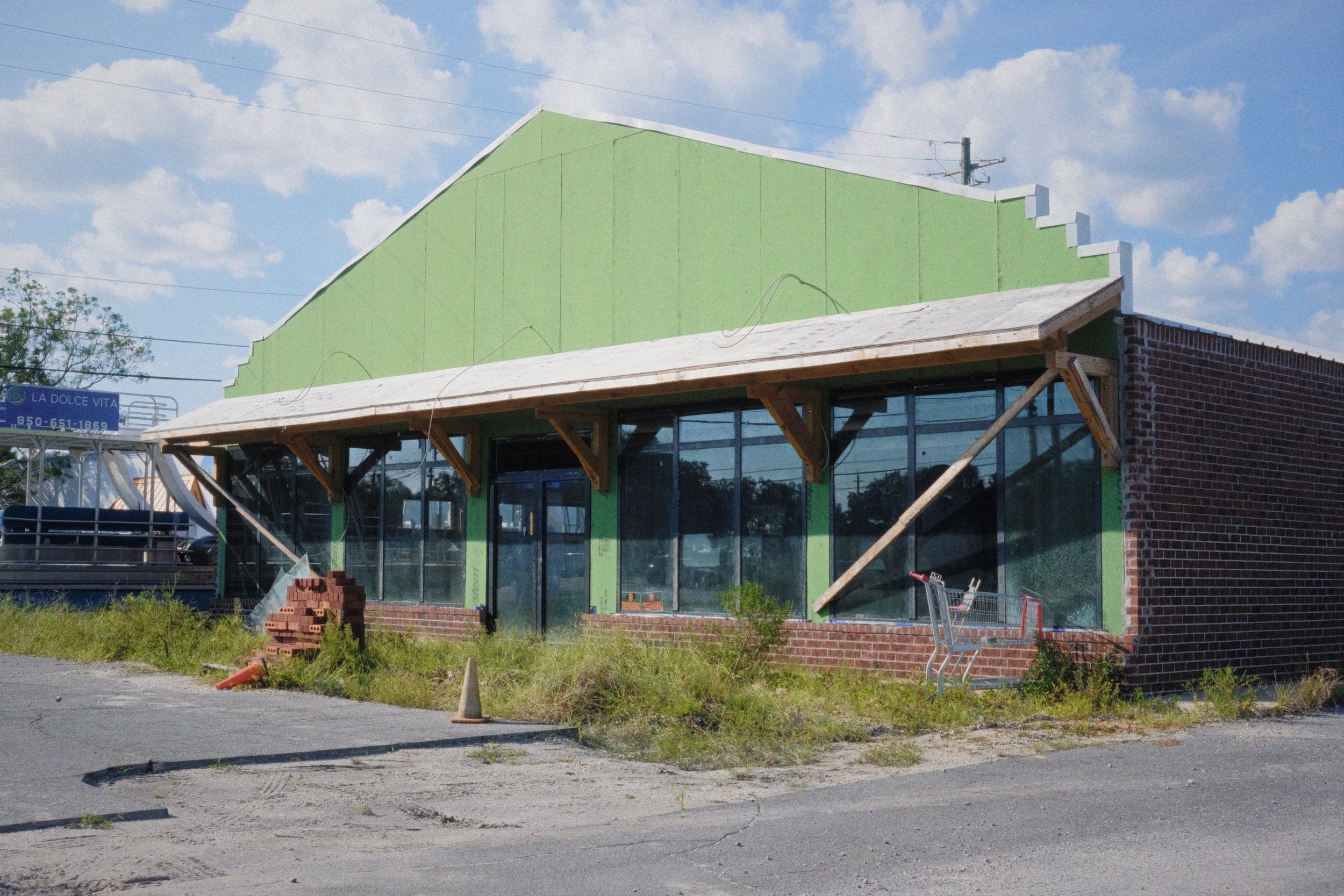 Dilapidated building with a shopping cart outside, under a blue sky with clouds.