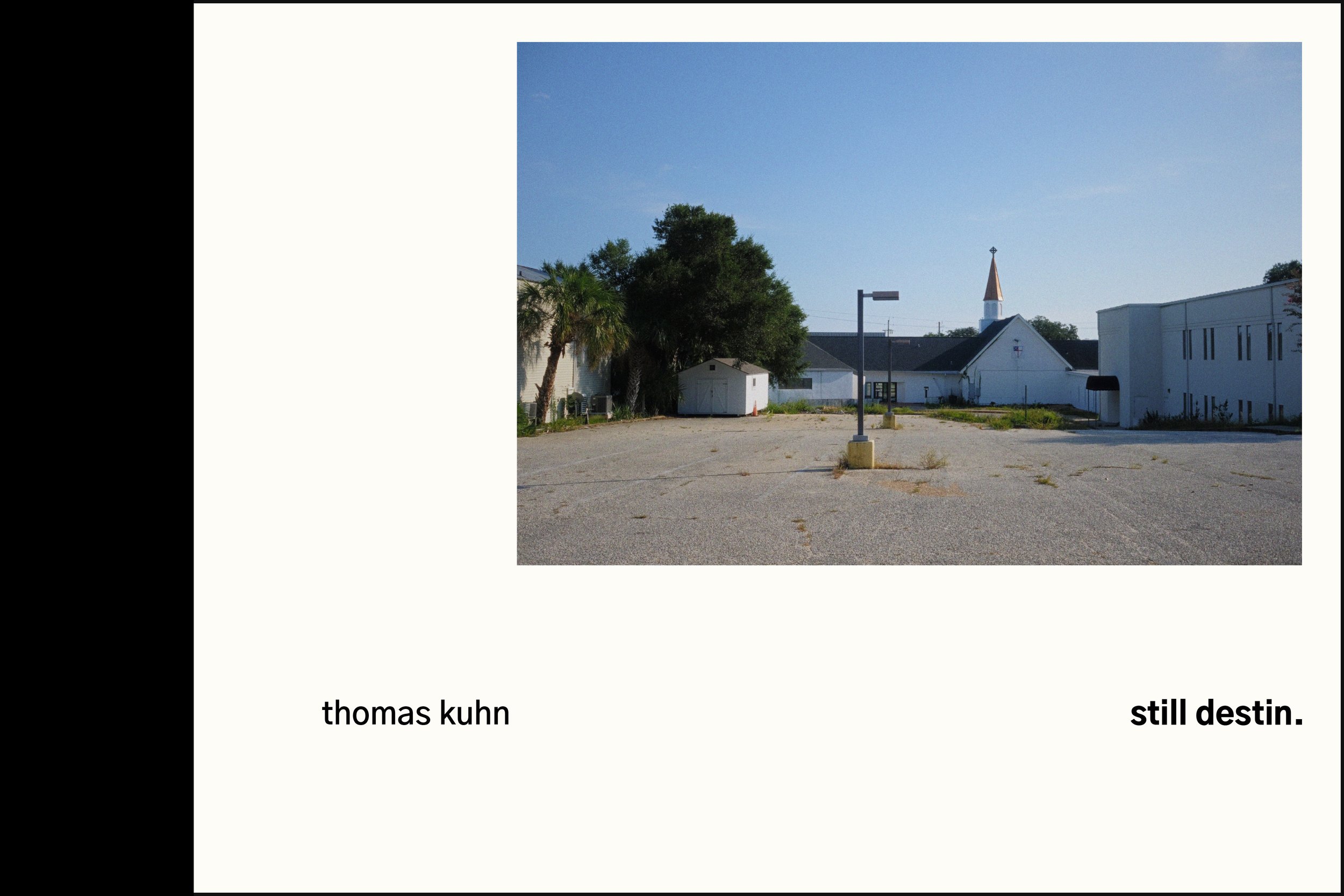 An image of an empty parking lot in front of white buildings, including a church with a steeple, under a clear blue sky with a few trees and a streetlight. The words "thomas kuhn" and "still destin." are written in a san serif typeface outside and be