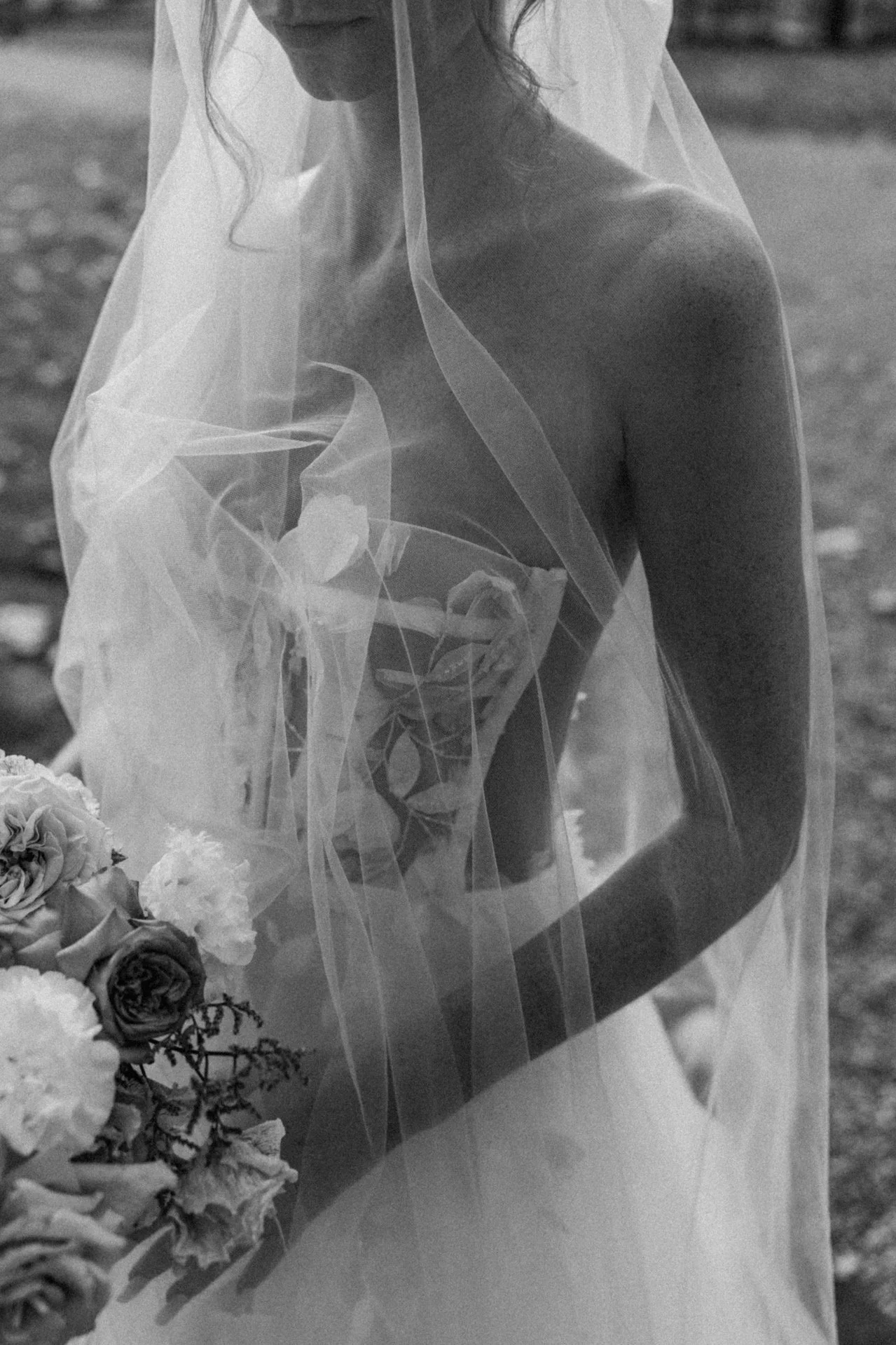 A woman wearing a wedding dress or veil, with flowers nearby, in a black-and-white photograph.