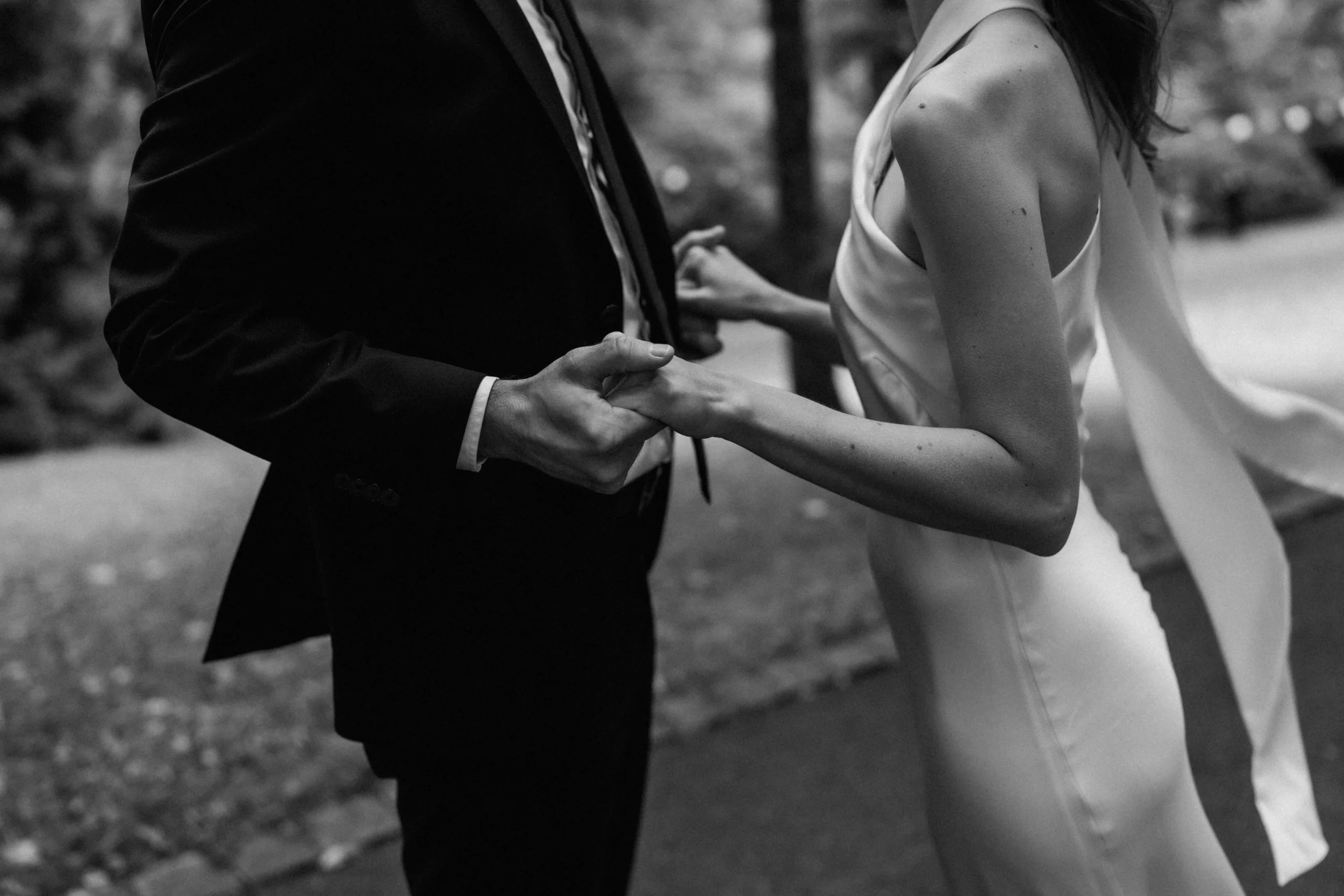 A close-up of a man and woman holding hands, dressed in formal clothing, outdoors.