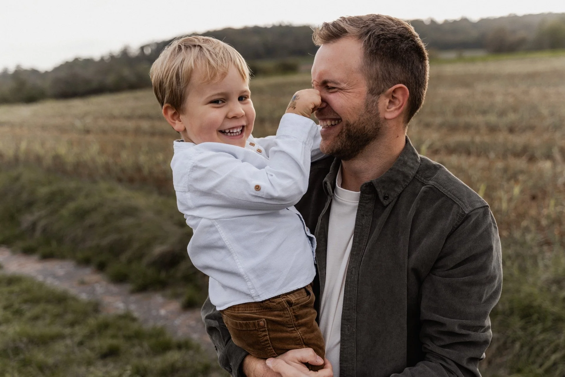 A man holding a smiling young boy in an outdoor field, playing and smiling together.