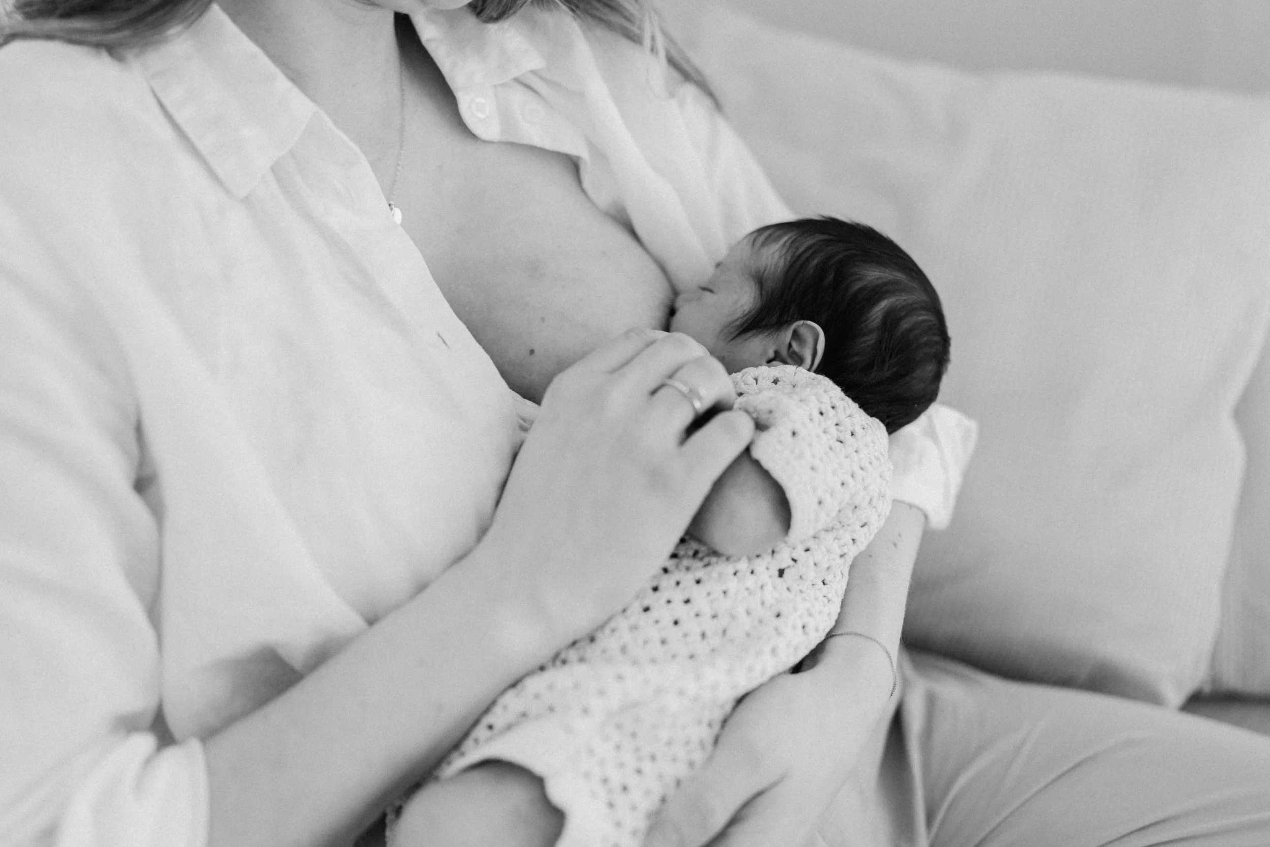 A woman breastfeeding a baby, wrapped in a crocheted blanket, in a close-up black and white photograph.