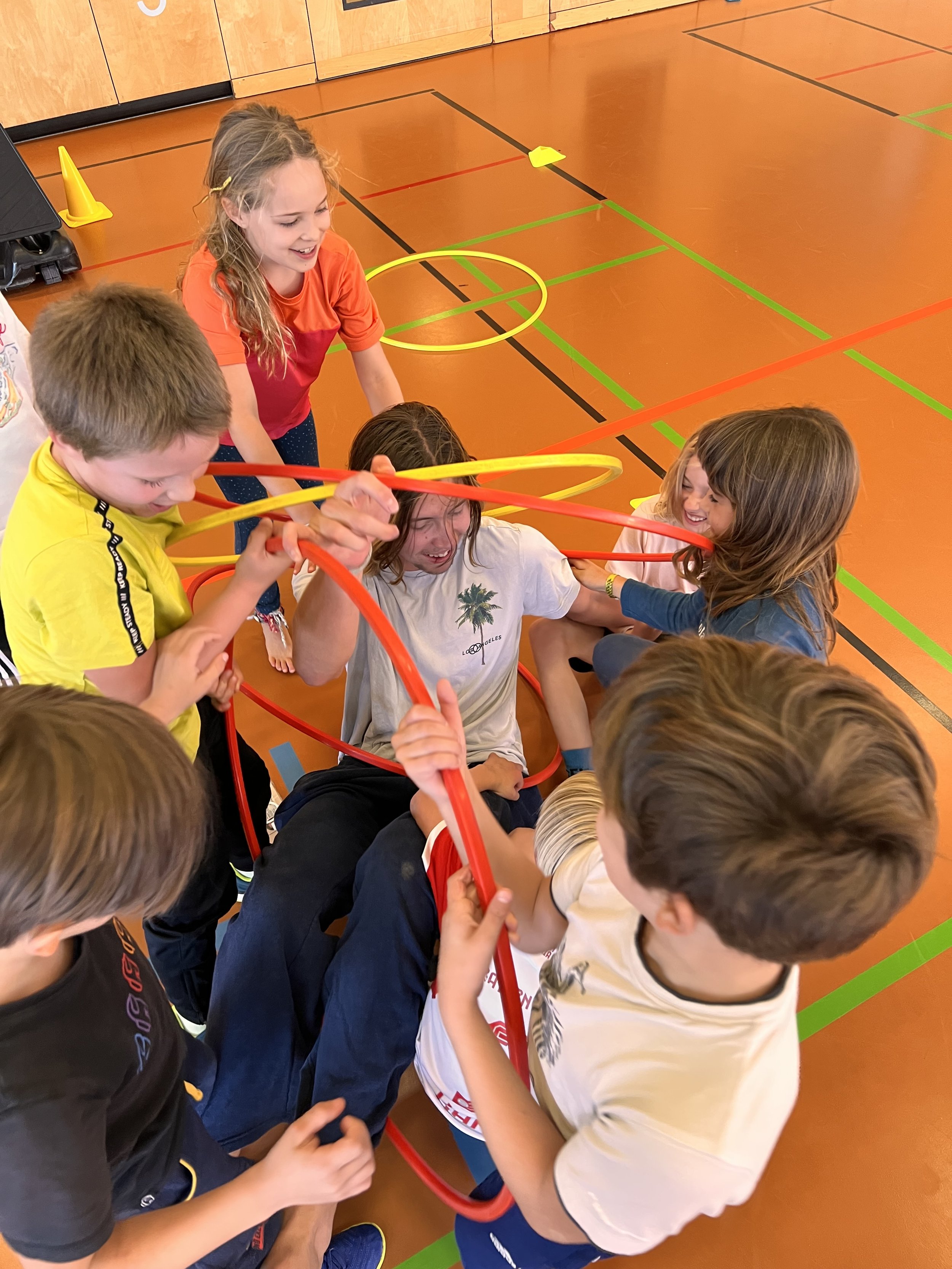 Junge und Mädchen spielen in einer Turnhalle mit bunten Plastikringen.