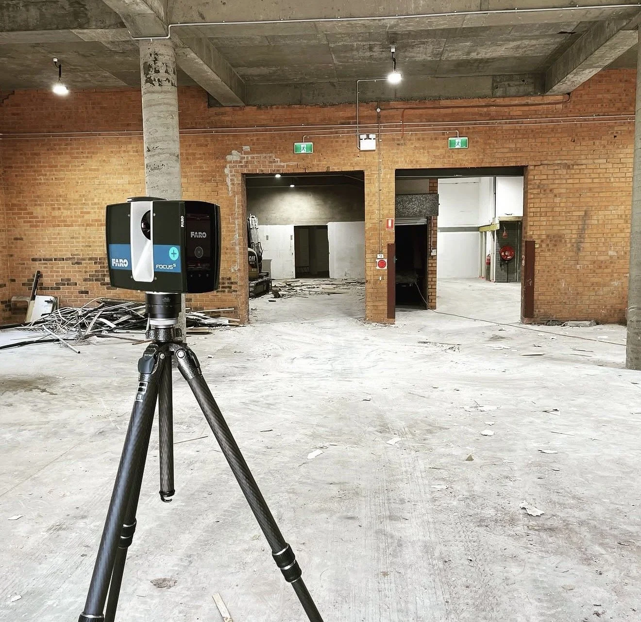 Innenansicht eines unvollendeten Gebäudes mit rotem Ziegelmauerwerk, Baustellenmaterialien und einem stationären 3D-Laserscanner auf einem Dreifuß, die Räume sind offen mit sichtbaren Lichtinstallationen.