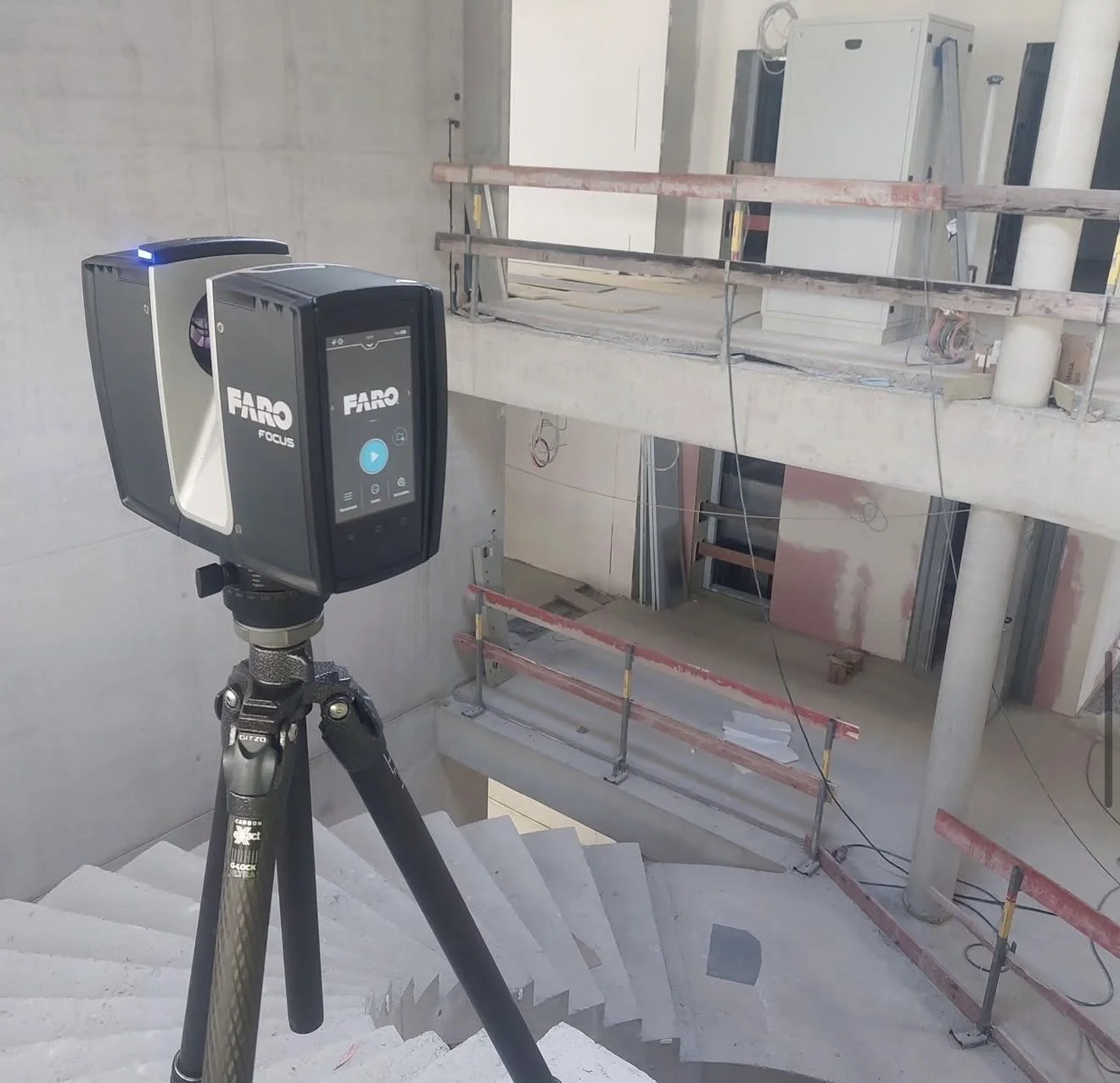 Baustelle mit Messgerät auf Dreibein, noch keine fertigen Einrichtungen, Baugerüst und Bauleiter in einem mehrstöckigen Gebäude.