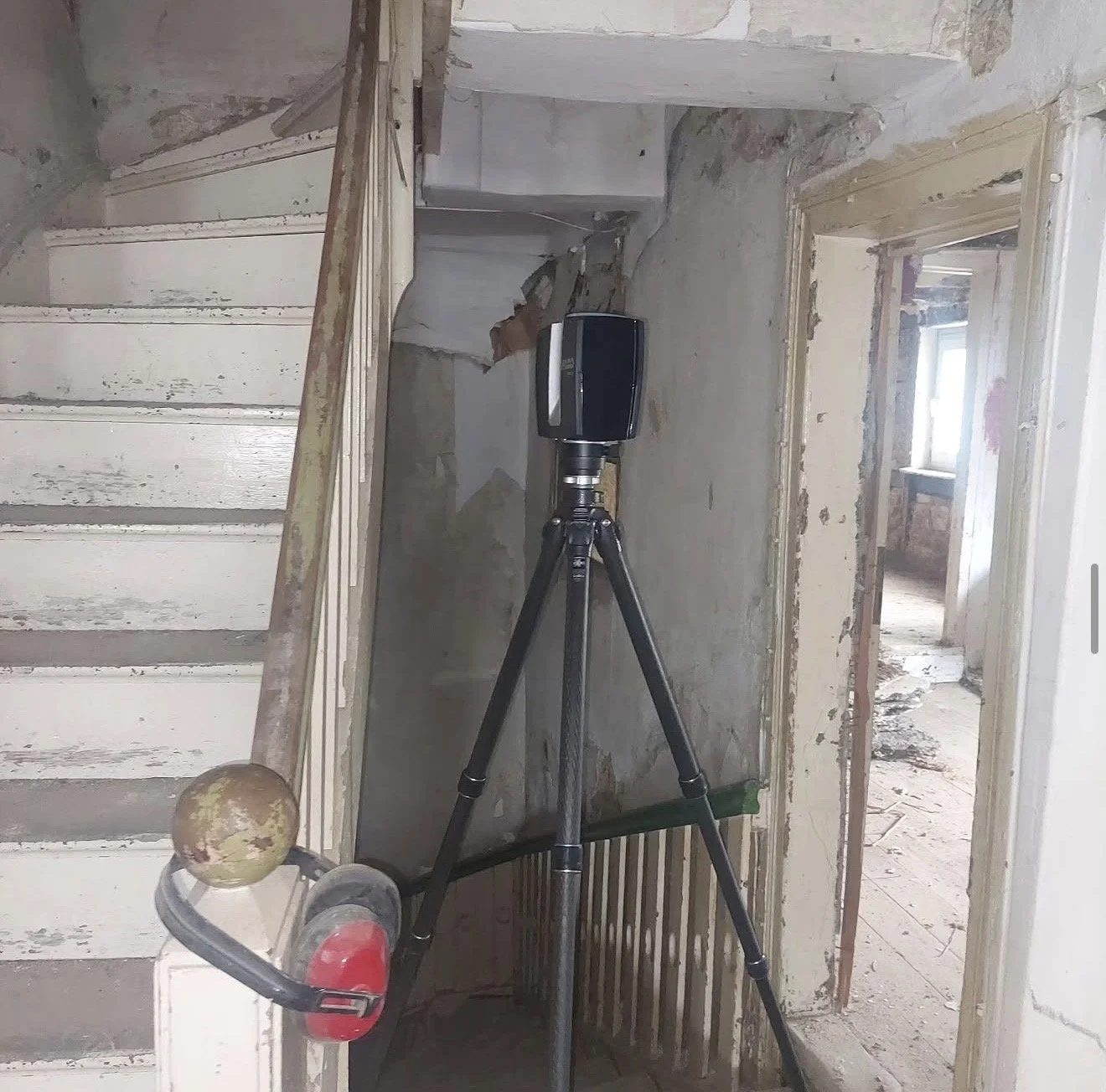 Innenaufnahme eines renovierungsbedürftigen Hauses mit einer Wartungskamera auf einem Stativ in der Mitte, veralteten Wänden und einem offenen Raum im Hintergrund.