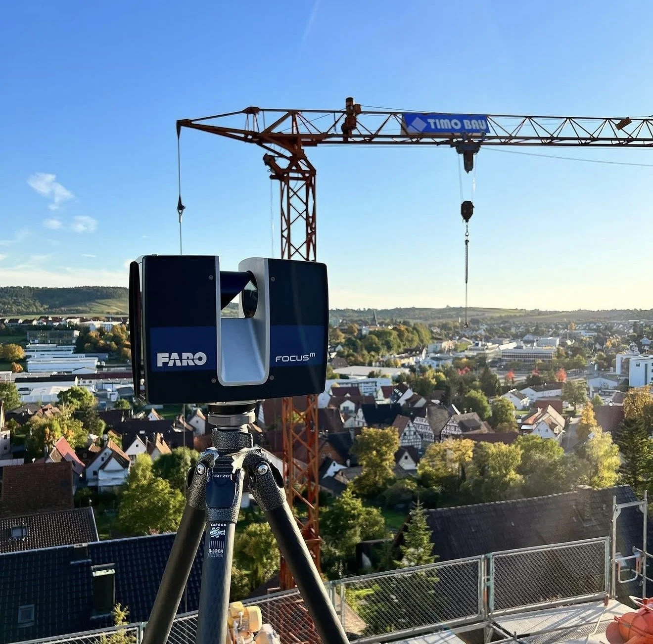 Aufnahme mit Vermessungsausrüstung auf einer Baustelle mit Blick auf eine Stadt und einen Kran im Hintergrund bei Sonne und blauem Himmel.