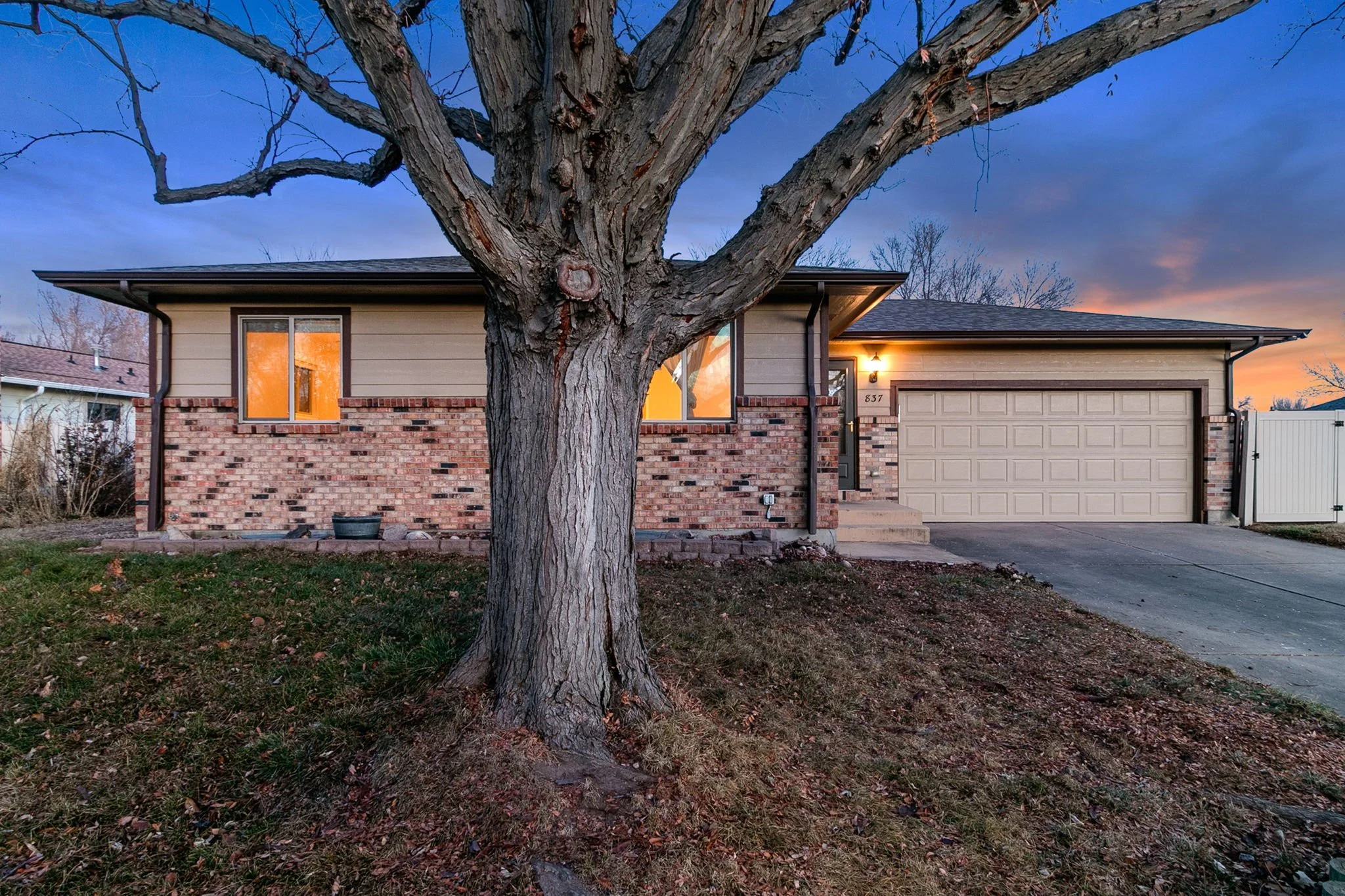 Front of a suburban house with a large tree in the yard during sunset.