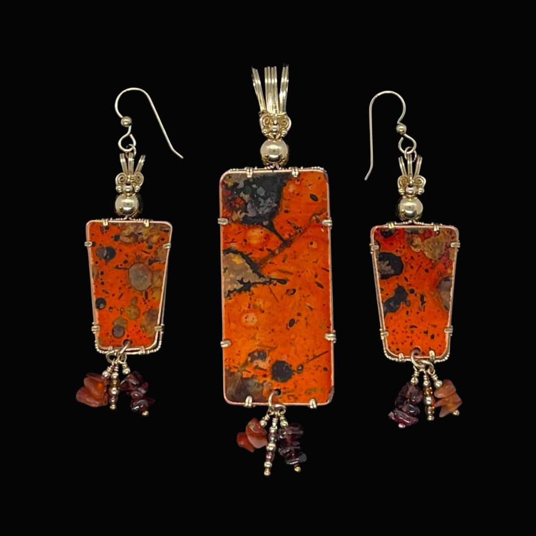 A matching set of jewelry including a pendant and earrings featuring rectangular orange stones with black and brown speckles, set in silver with dangling dark red and orange beads.