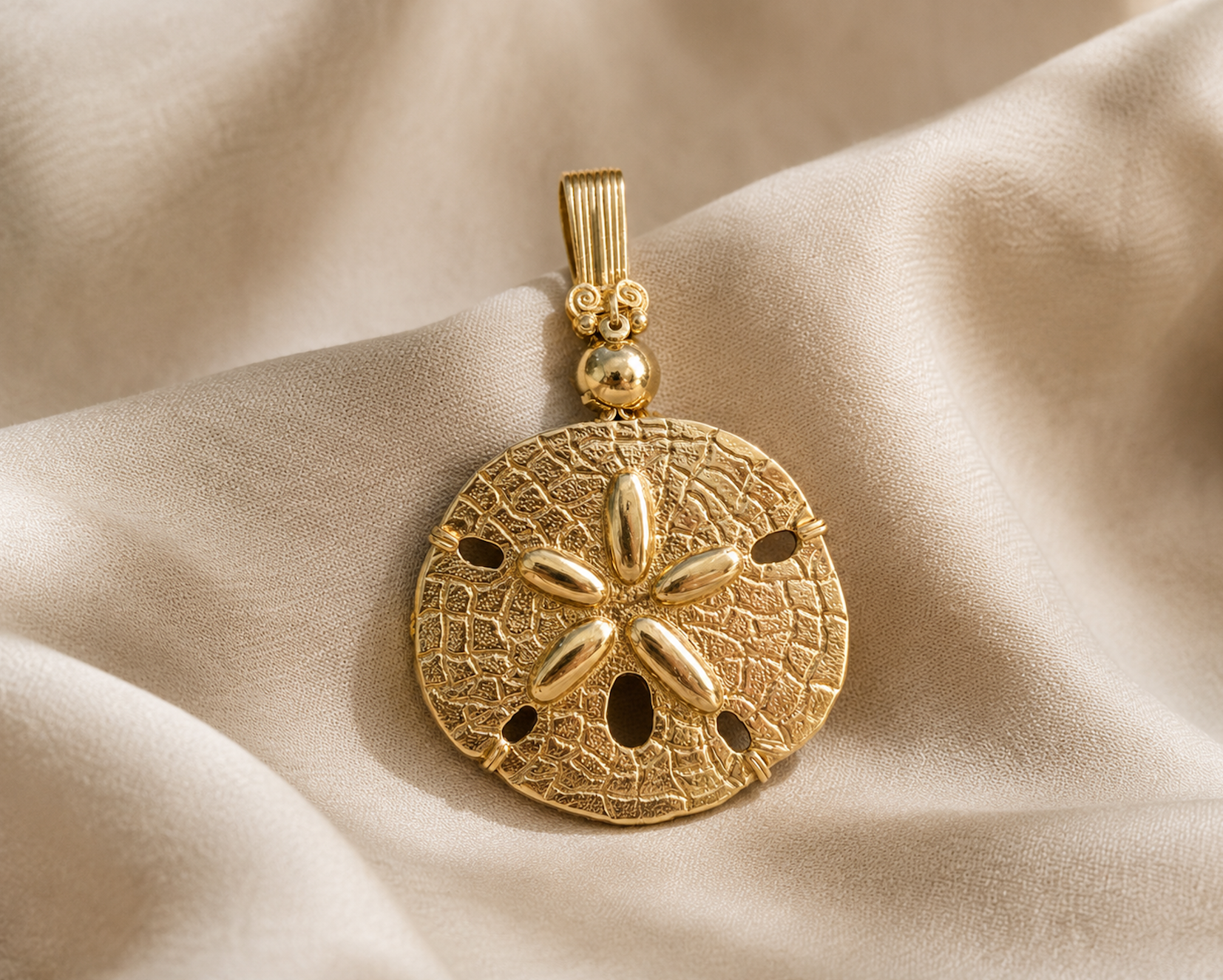 Gold sand dollar pendant with a decorative circular design, embedded with oval-shaped gold accents, placed on cream-colored fabric.