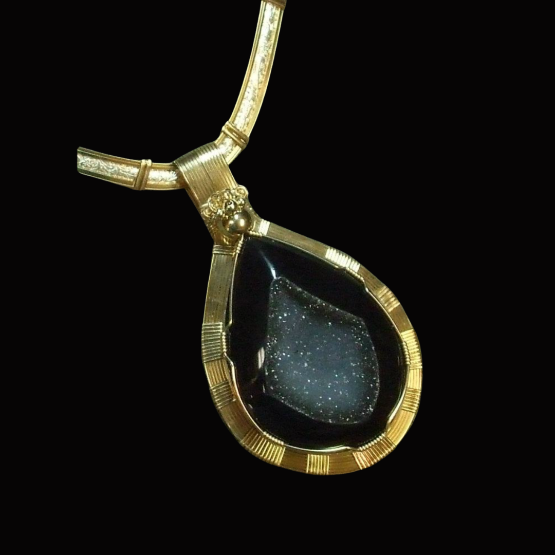 Gold and black gemstone necklace with a teardrop pendant, set against a black background.