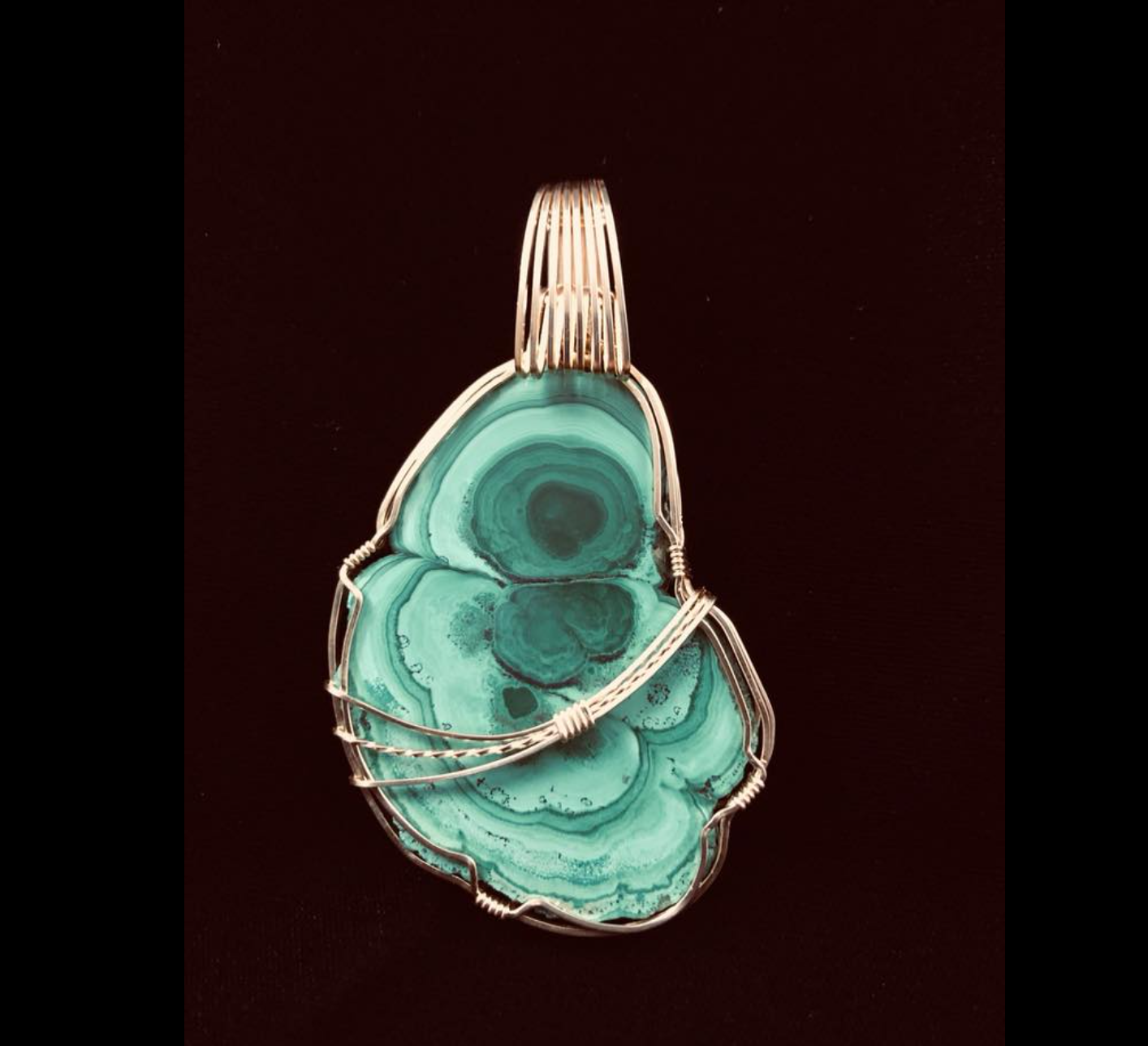 Handmade jewelry piece with a large green-blue Malakite stone wrapped in gold wire.