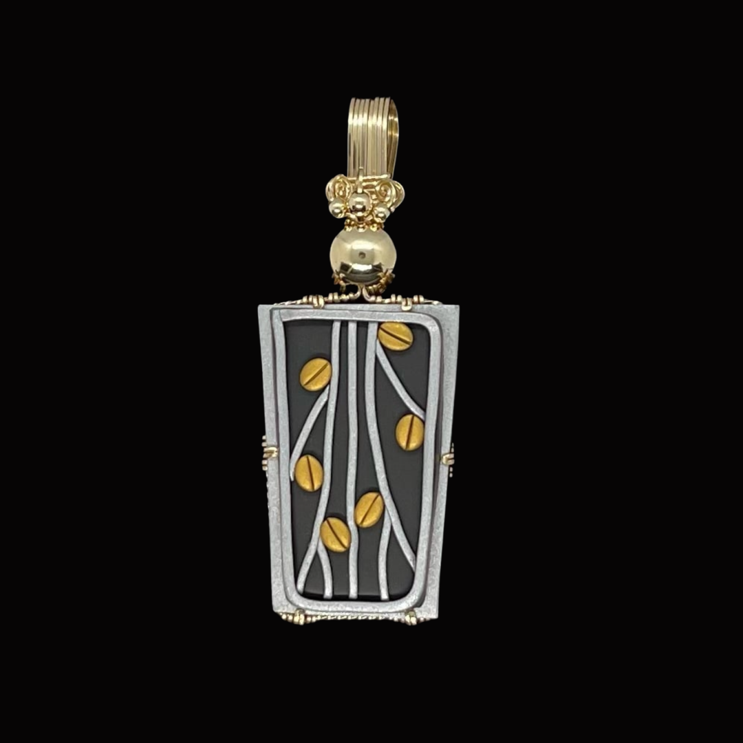 A pendant jewelry piece with a rectangular frame featuring a floral and vine design, adorned with small gold accents on a black background.