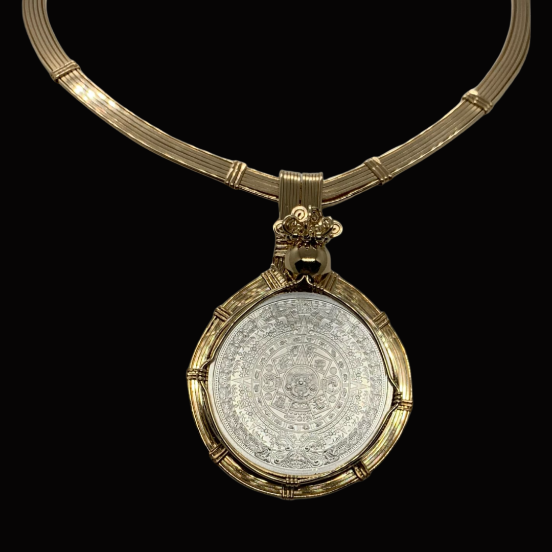 Gold necklace with a large circular pendant featuring intricate symbols and designs, set against a black background.