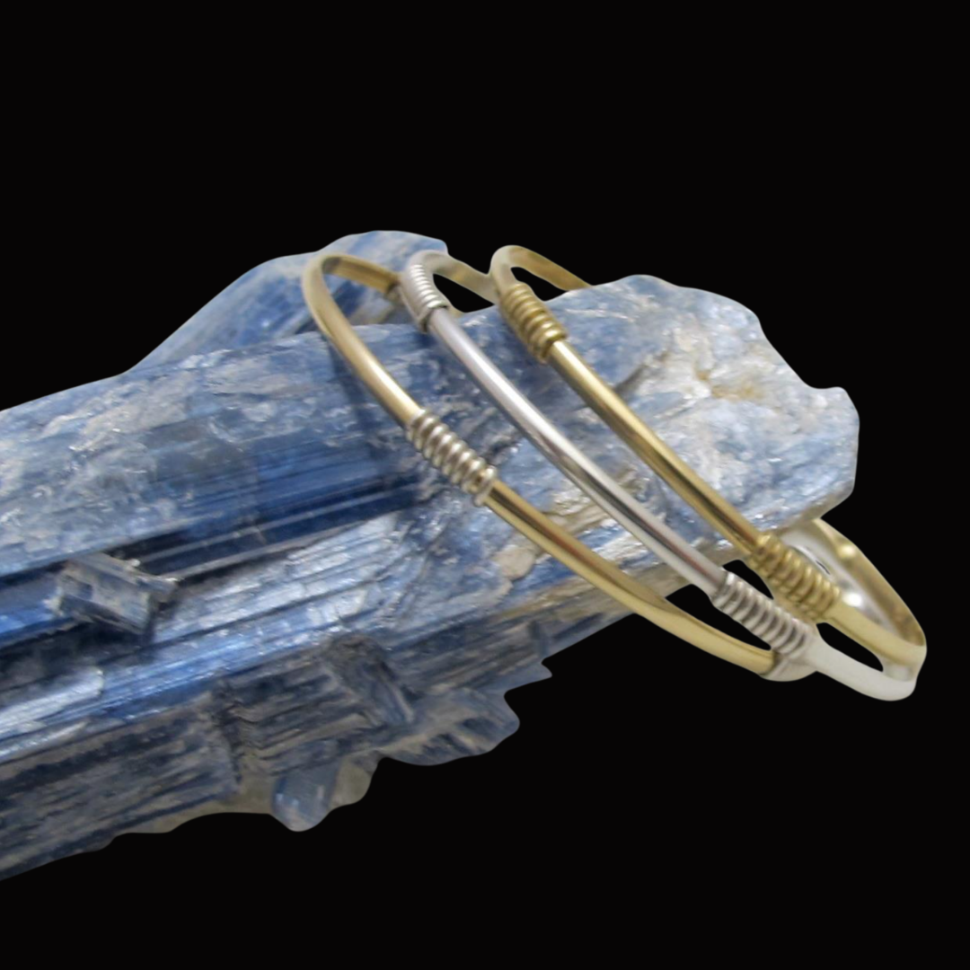Three metallic bangles resting on a blue marbled stone against a black background.
