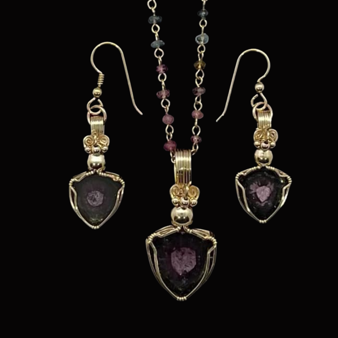 Set of jewelry including a pair of earrings and a necklace, all featuring dark purple stones with pink inclusions, set in silver with decorative wire wrapping, against a black background.