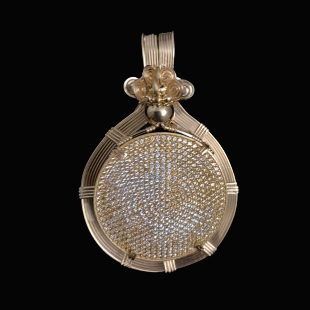 A gold pendant with a textured, circular center encrusted with small diamonds, featuring an intricate design at the top against a black background.