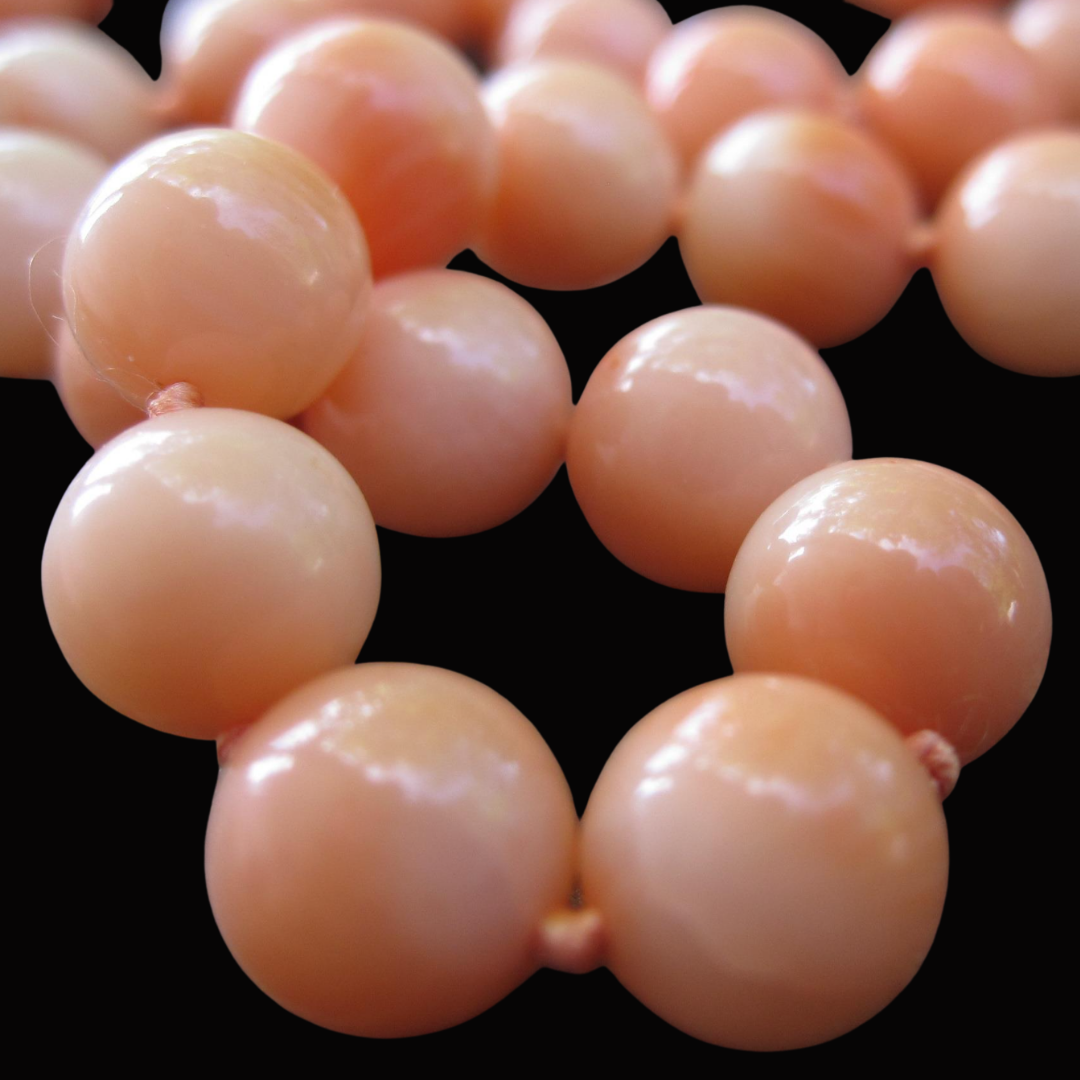 Close-up of a peach-colored pearl necklace arranged in a circle on a black background.