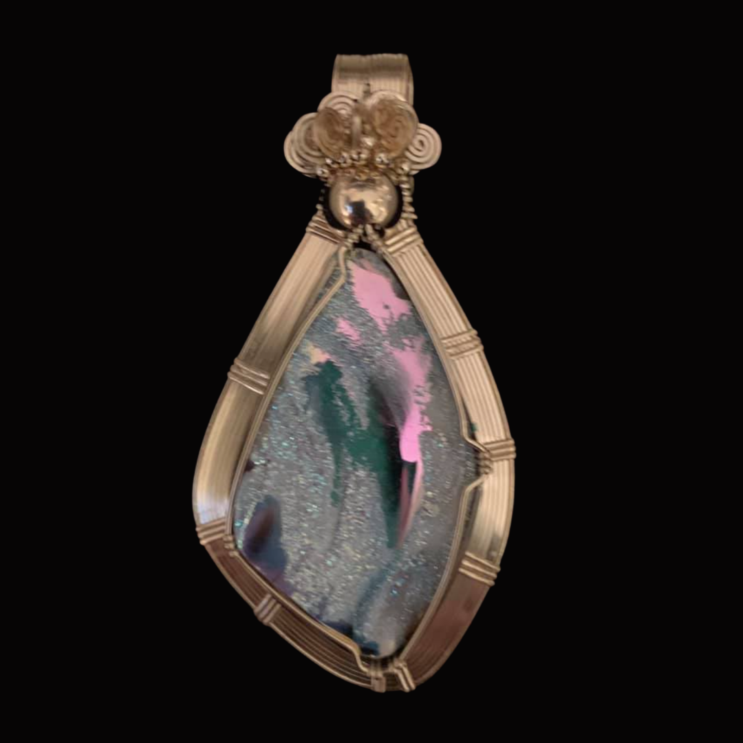 Close-up of a pendant with a glittery, abstract design and a pink silhouette on a black background.