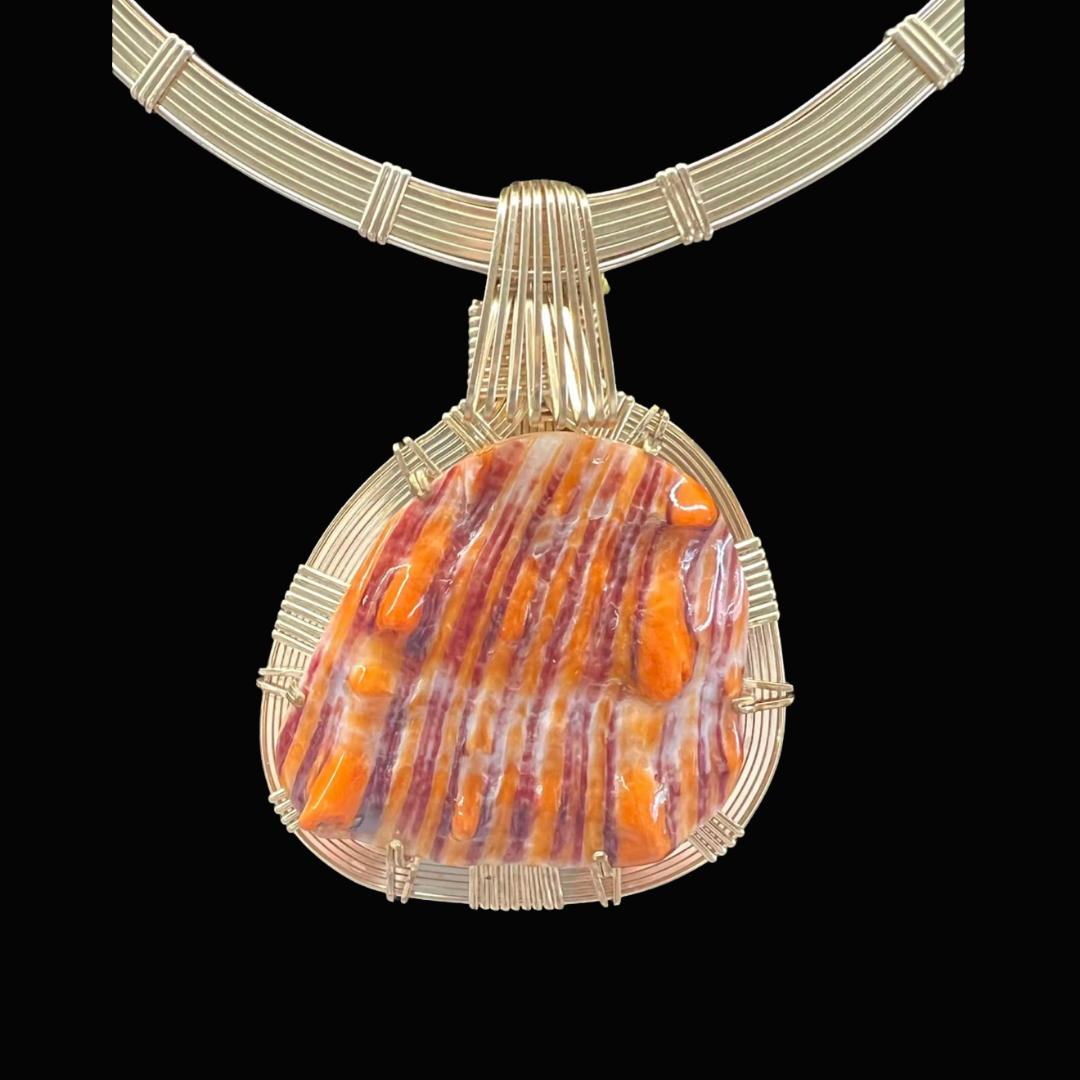 A pendant necklace featuring a large, colorful gemstone with orange, purple, and cream stripes, set in a silver wire frame, displayed against a black background.
