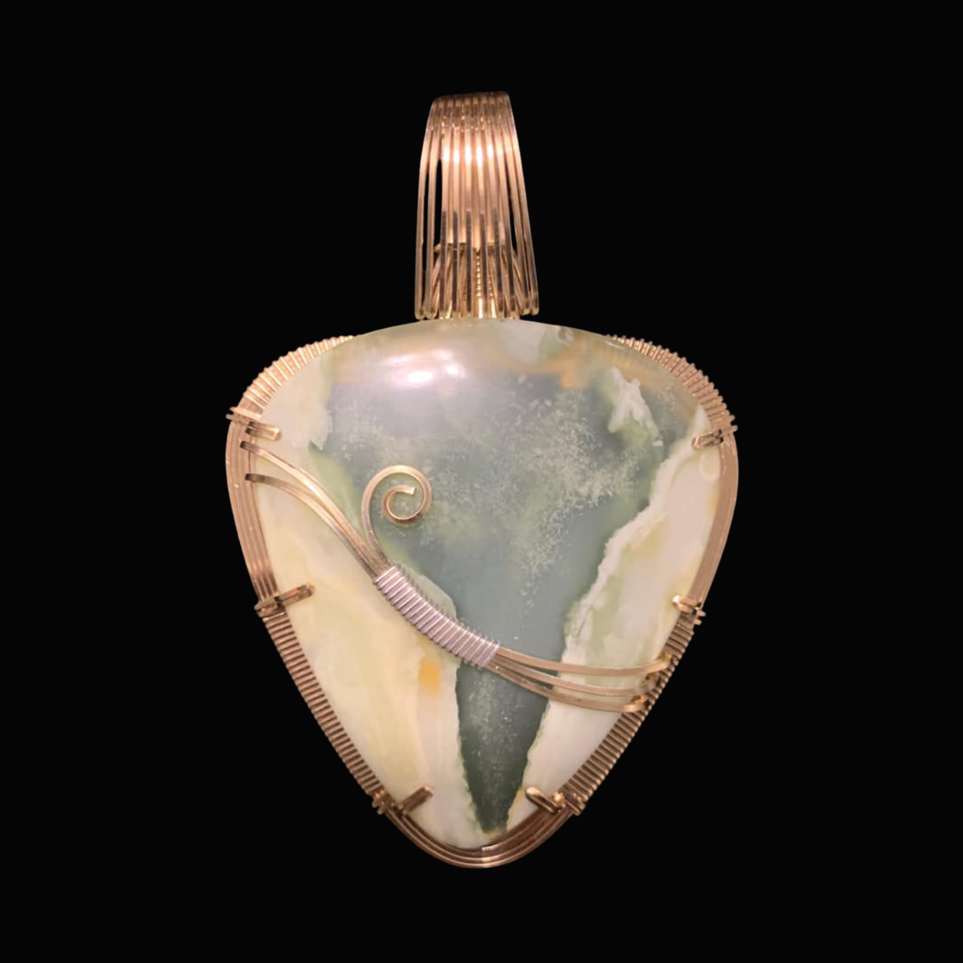 A heart-shaped pendant made of a semi-precious stone with gold wire wrapping and a gold bail on a black background.