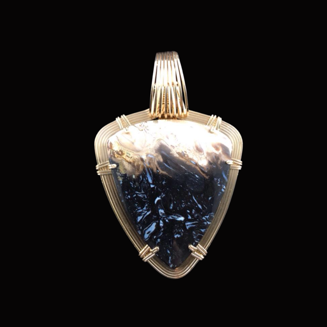 A pendant necklace with a large, polished black and white stone set in a gold wire frame against a black background.