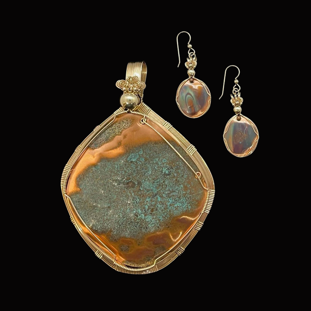 Gold pendant necklace with a large, oval-shaped, multicolored stone and matching earrings against a black background.