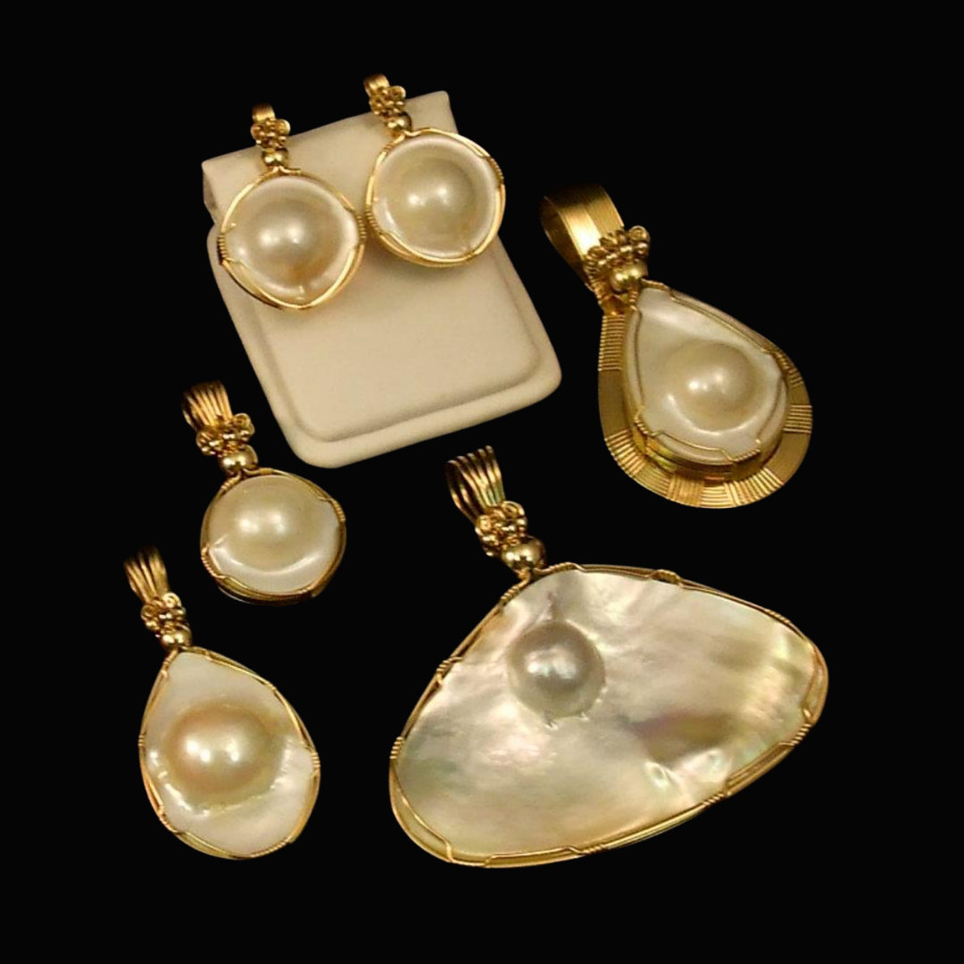 Set of gold jewelry featuring large pearl pendants and earrings displayed on a black background.