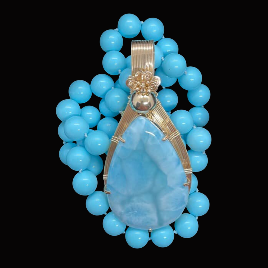 Decorative necklace with large blue beads and a teardrop-shaped blue gemstone pendant set in gold.
