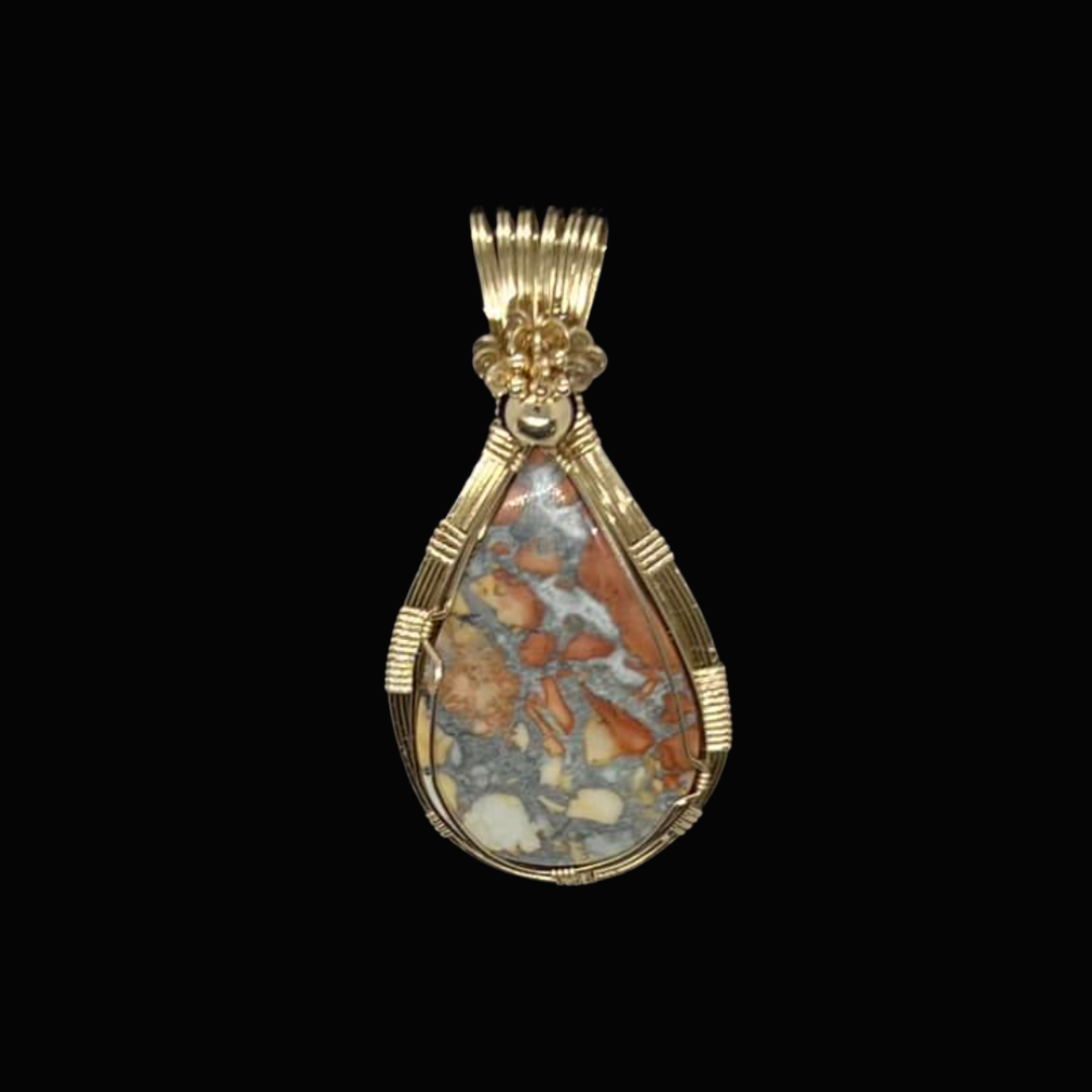 Gold pendant with an oval multicolored stone, possibly jasper, set in a decorative gold wire wrap against a black background.