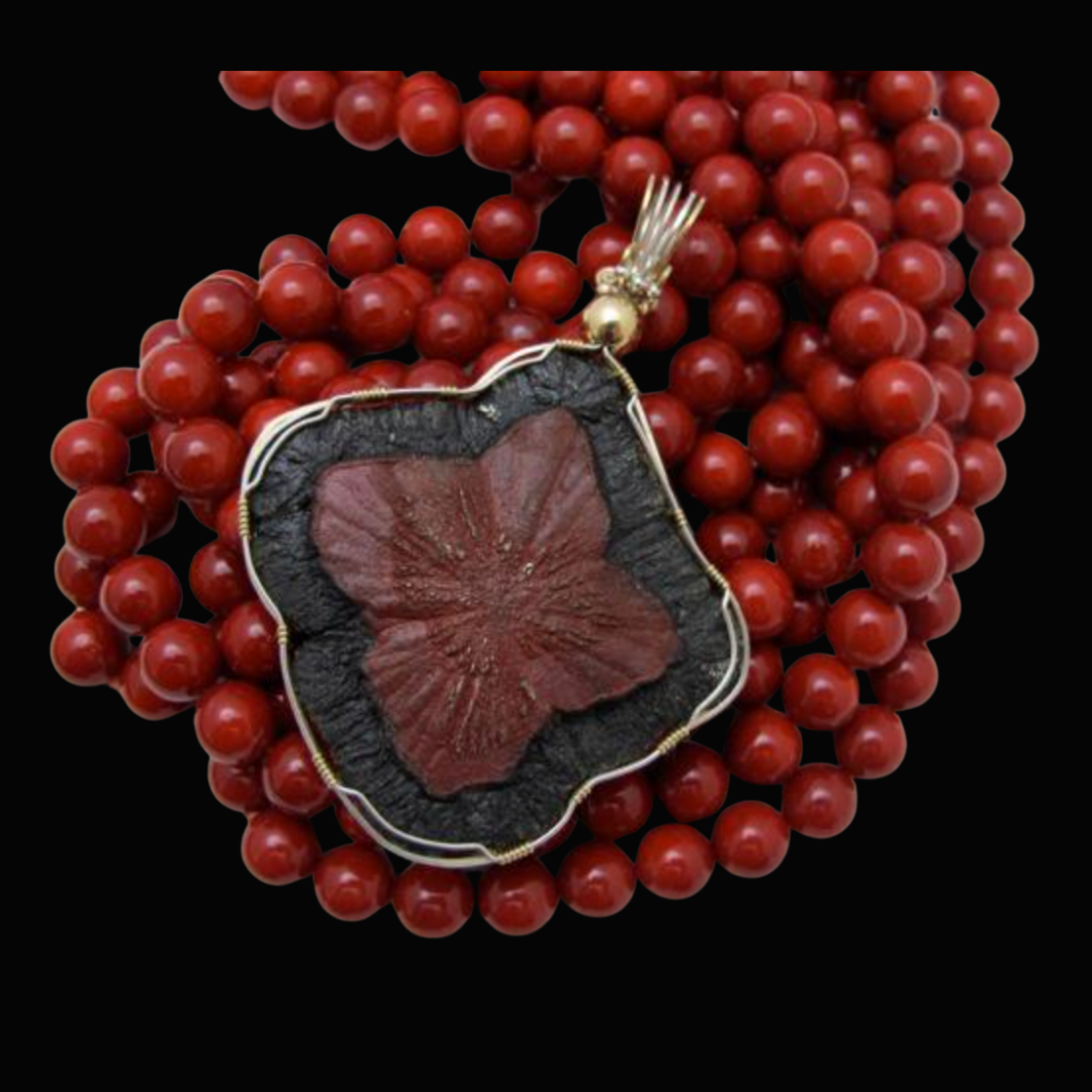 Close-up of a red beaded necklace with a decorative pendant featuring a leaf motif, set against a black background.