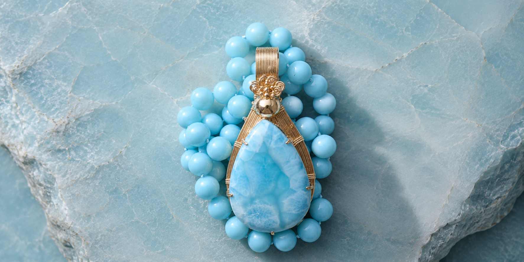 A piece of jewelry with a large teardrop-shaped blue stone set in gold wire, surrounded by blue beads, laid on a blue stone surface.