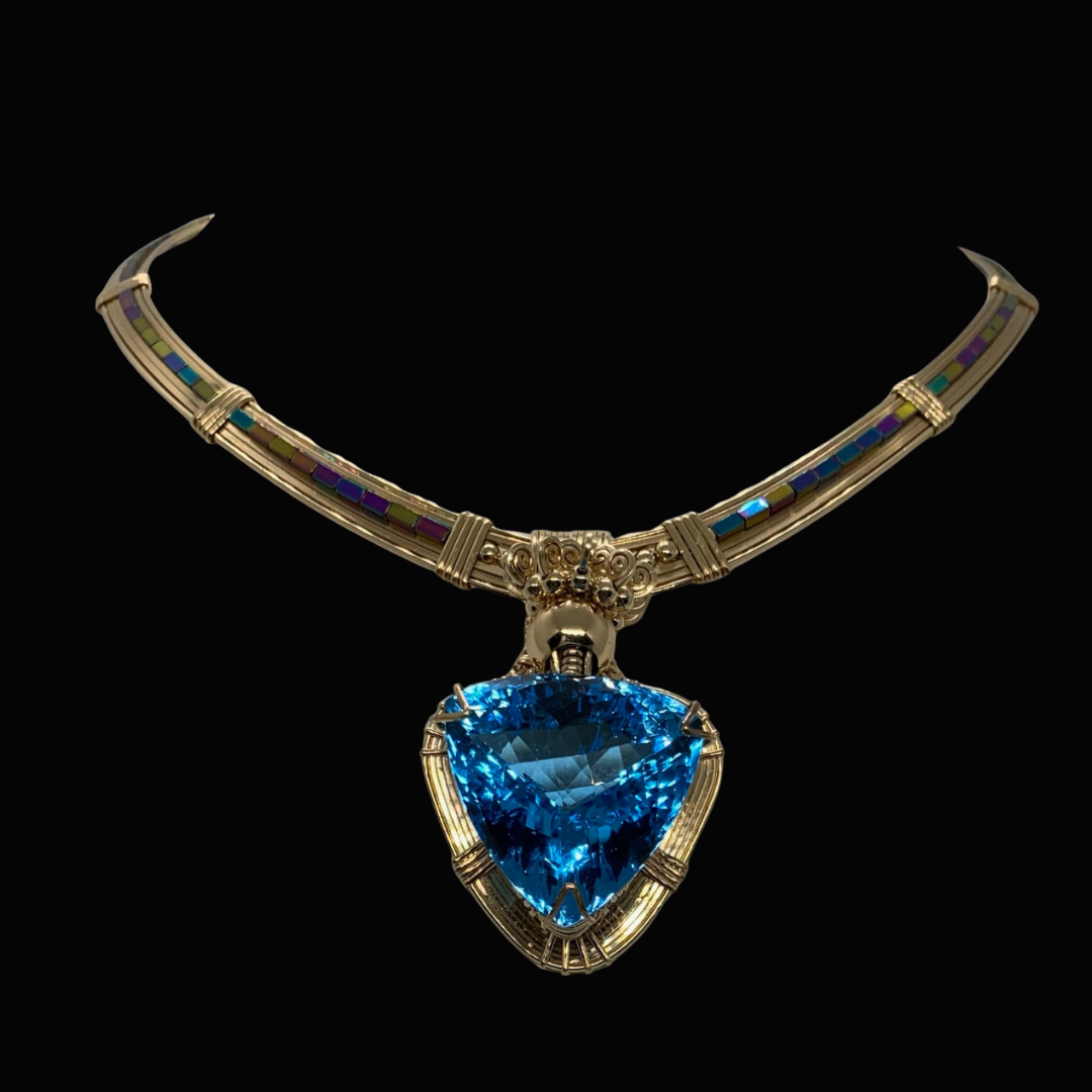 A gold necklace with colorful inlays and a large triangular blue gemstone pendant
