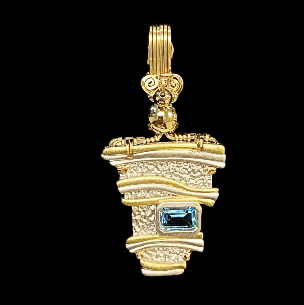 Gold and silver pendant with blue gemstone on a black background.