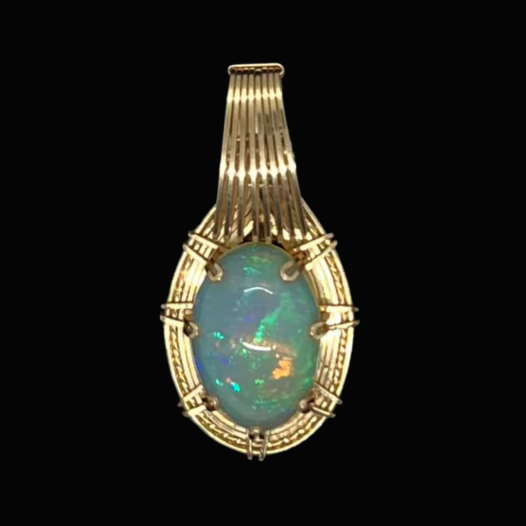 Gold pendant with an oval opal gemstone, set in an intricate gold frame, against a black background.