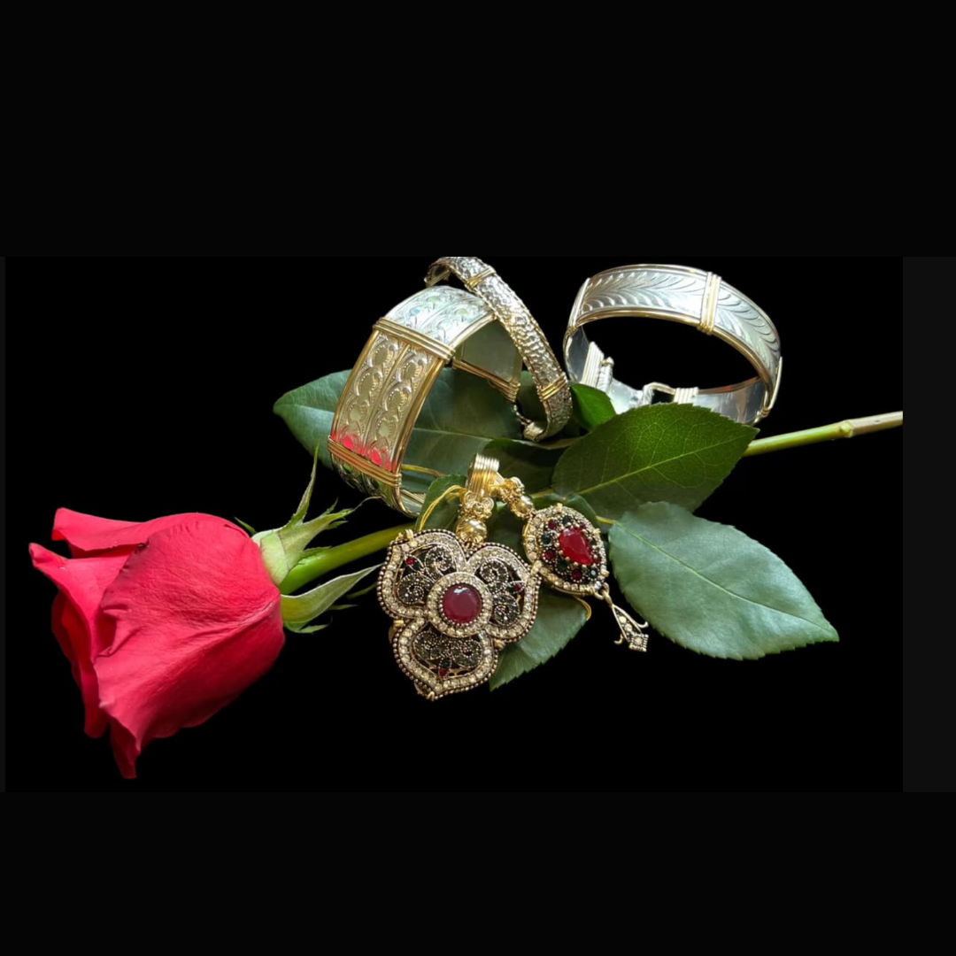 Jewelry including bangles, earrings, and a ring on a pink rose with green leaves against a black background.