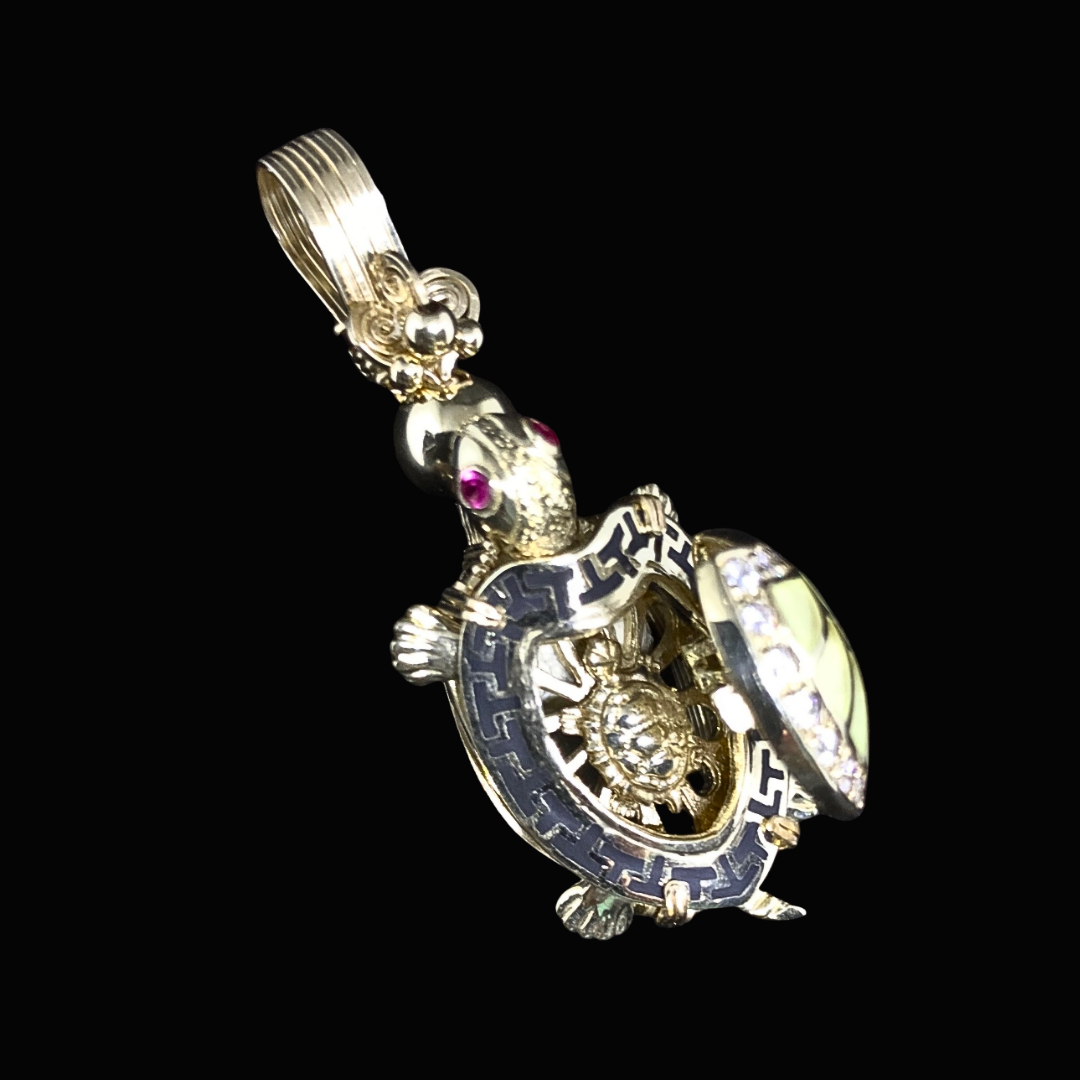 Gold turtle pendant with decorative details and pink gemstones as eyes, set against a black background.