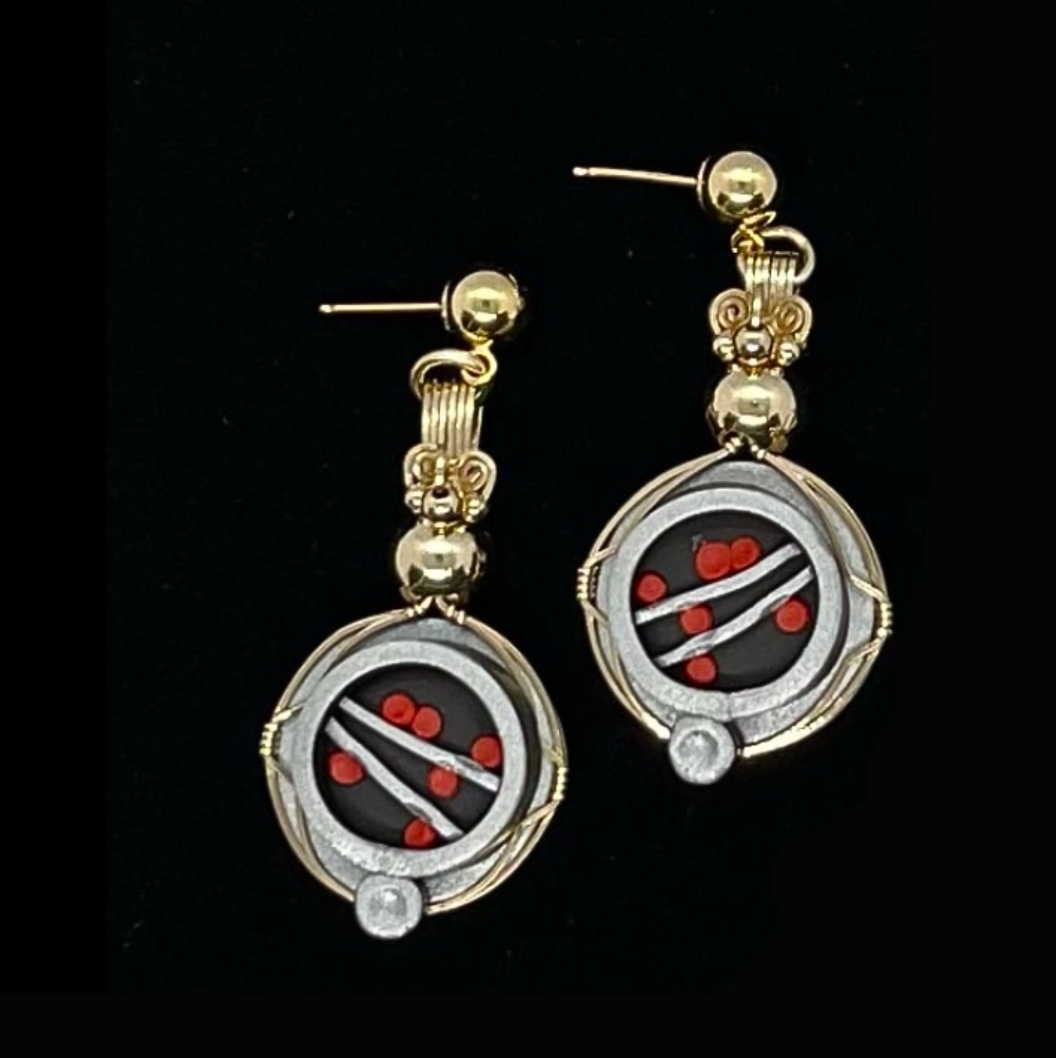 Gold and silver earrings with circular black, red, white, and clear gemstone design, lying on a black background.