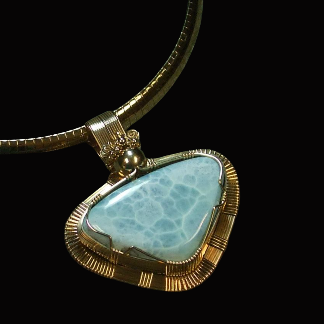 Gold necklace with a large, irregularly shaped, light blue gemstone pendant, set against a black background.