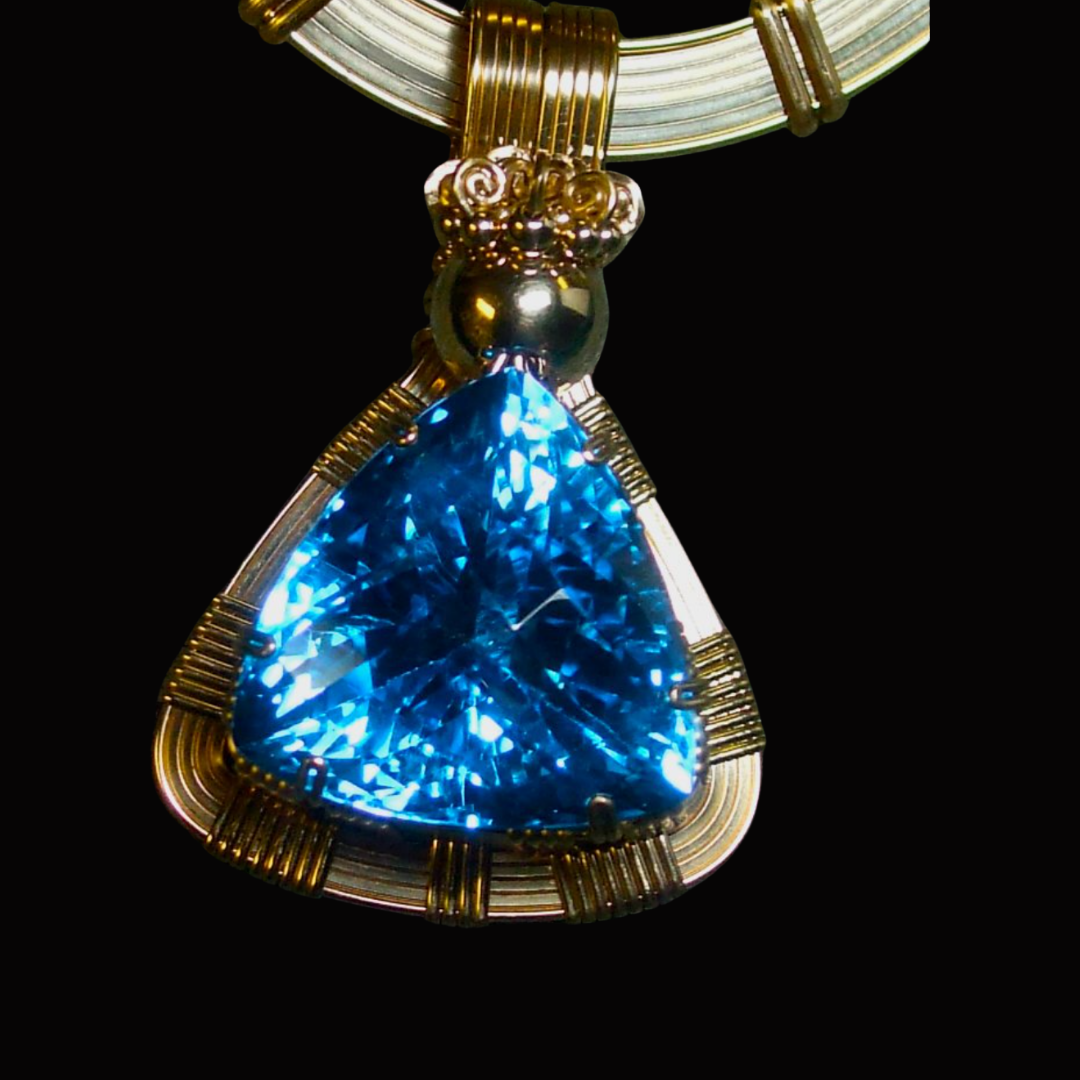 Close-up of a gold necklace with a large, blue, triangular gemstone pendant against a black background.