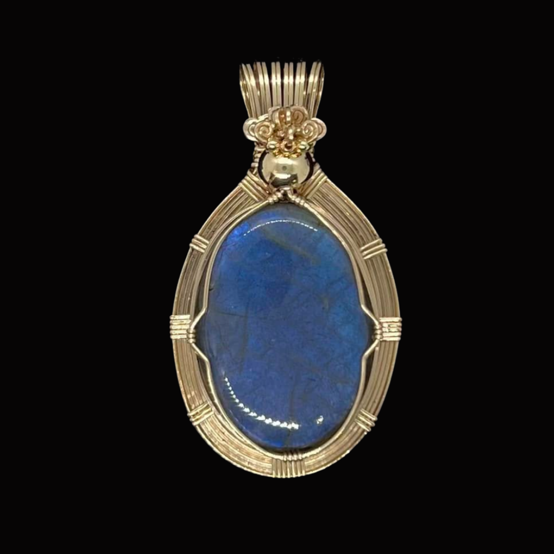 Gold pendant with a large blue oval gemstone set in the center, surrounded by intricate gold wire detailing, against a black background.