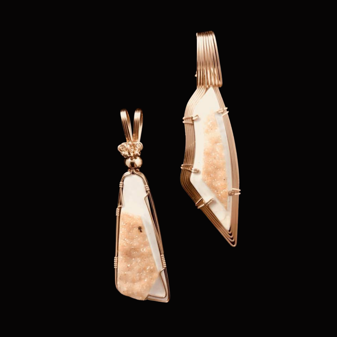 A pair of earrings with pinkish-beige stones wrapped in gold wire on a black background.