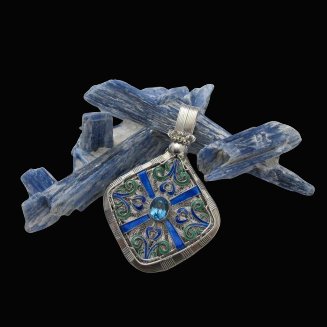 Silver pendant with blue and green decorative design and a large blue gemstone, resting on a cluster of blue and white mineral crystals on a black background.