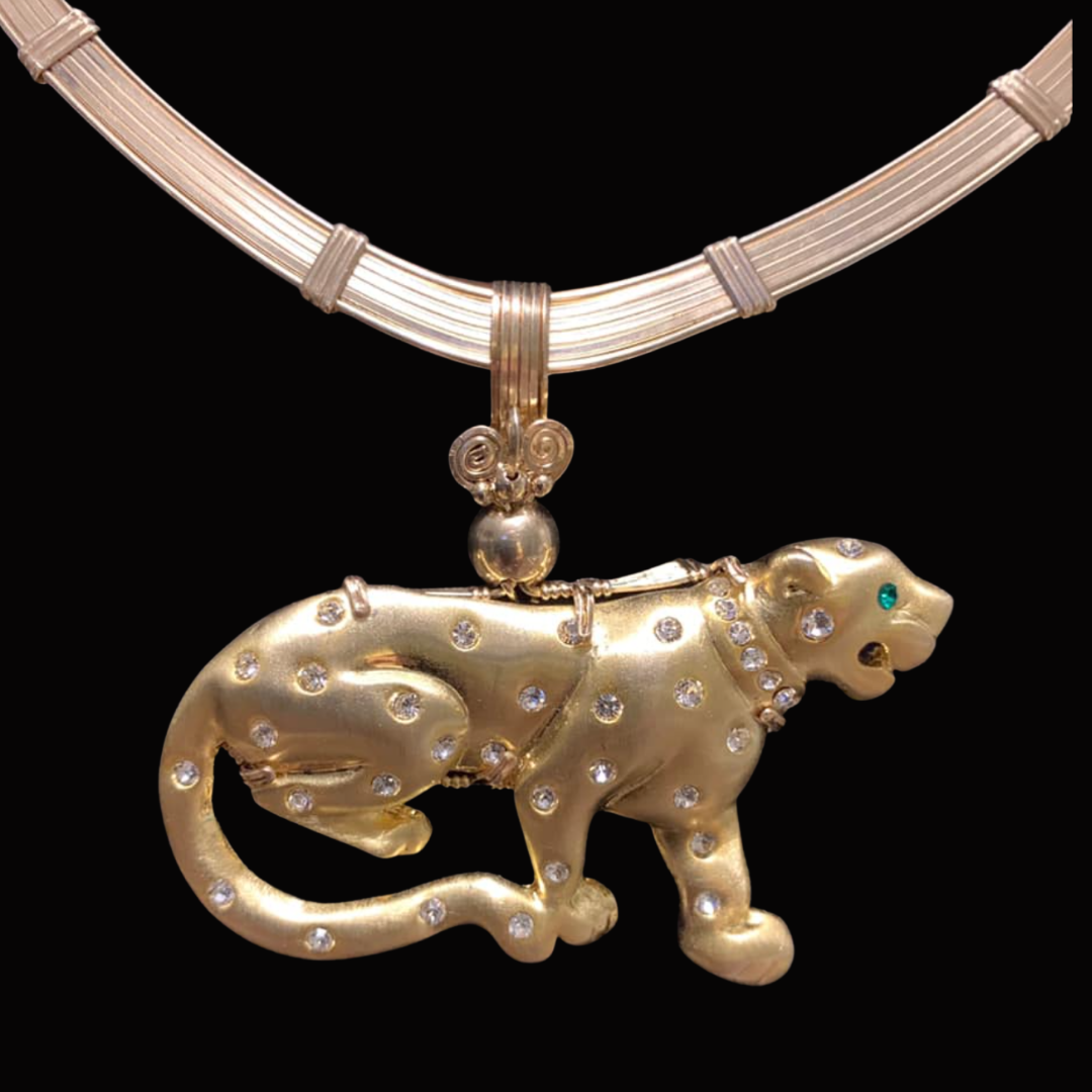 A gold necklace with a large panther pendant decorated with small diamonds and a green gemstone eye, mounted on a black background.