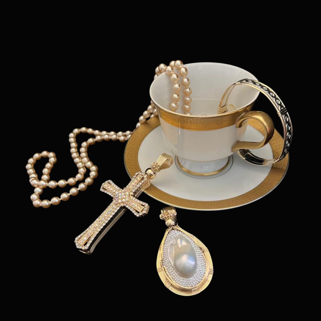 A decorative teacup and saucer with gold accents, surrounded by pearl jewelry including a pearl necklace, a pearl bracelet, a large pearl pendant, and a gold cross pendant, set against a black background.