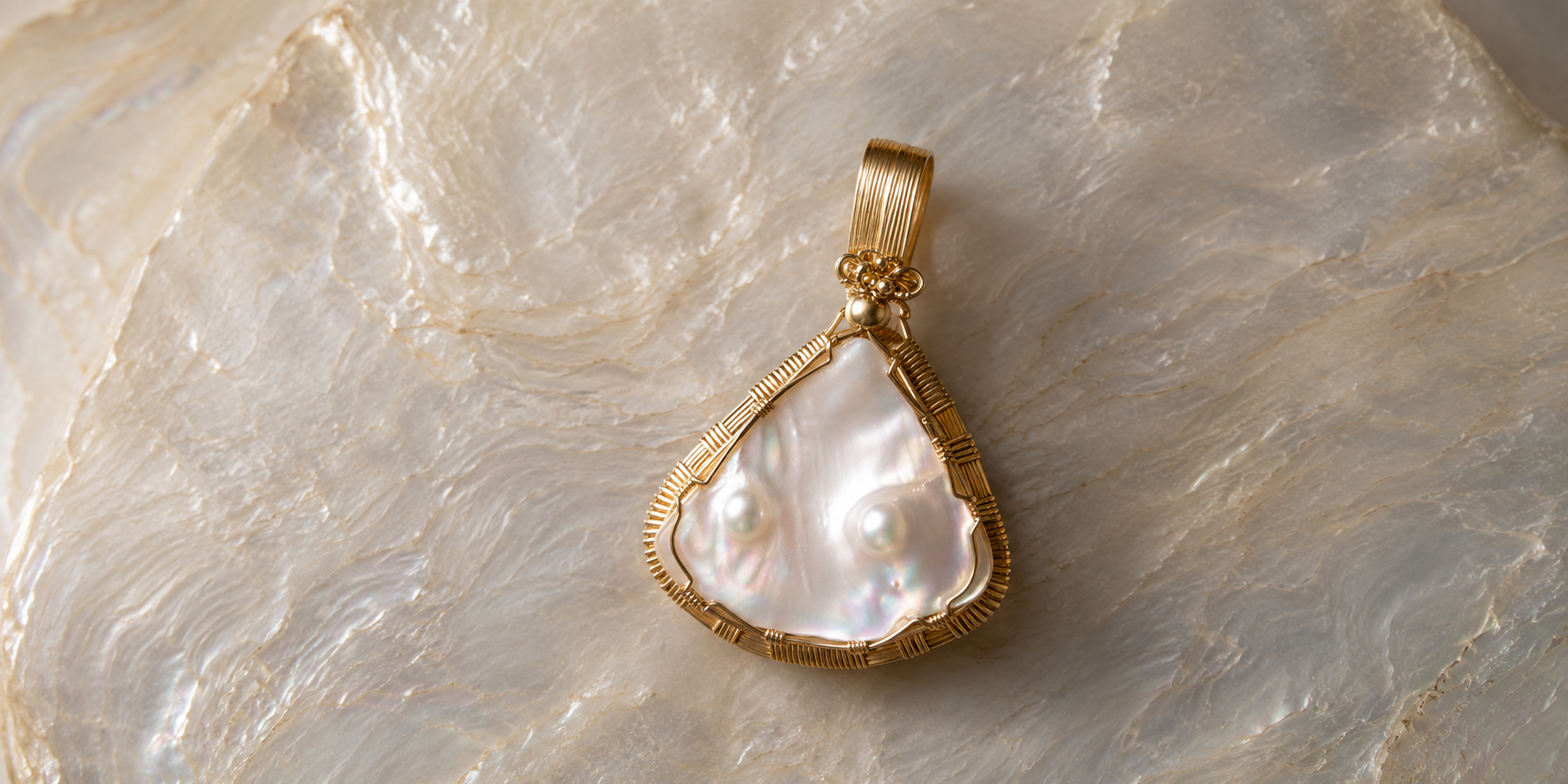 Gold pendant with a large, irregularly shaped pearl, resting on a textured, iridescent surface.